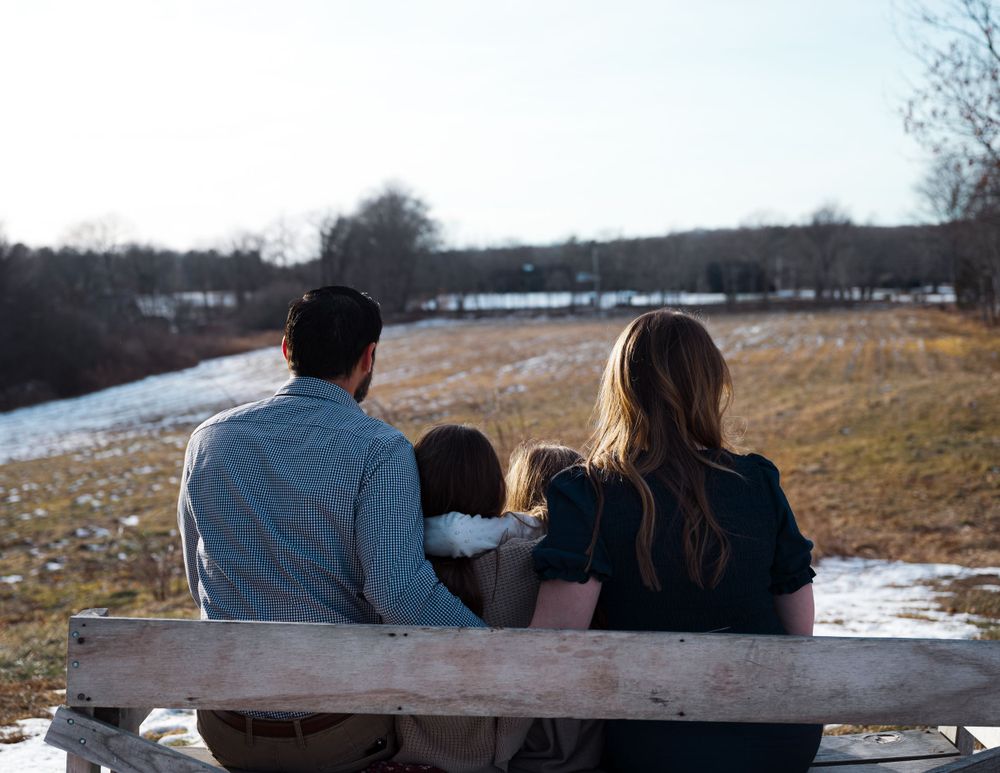 Family sitting together on wooden log at sunset in snowy field.