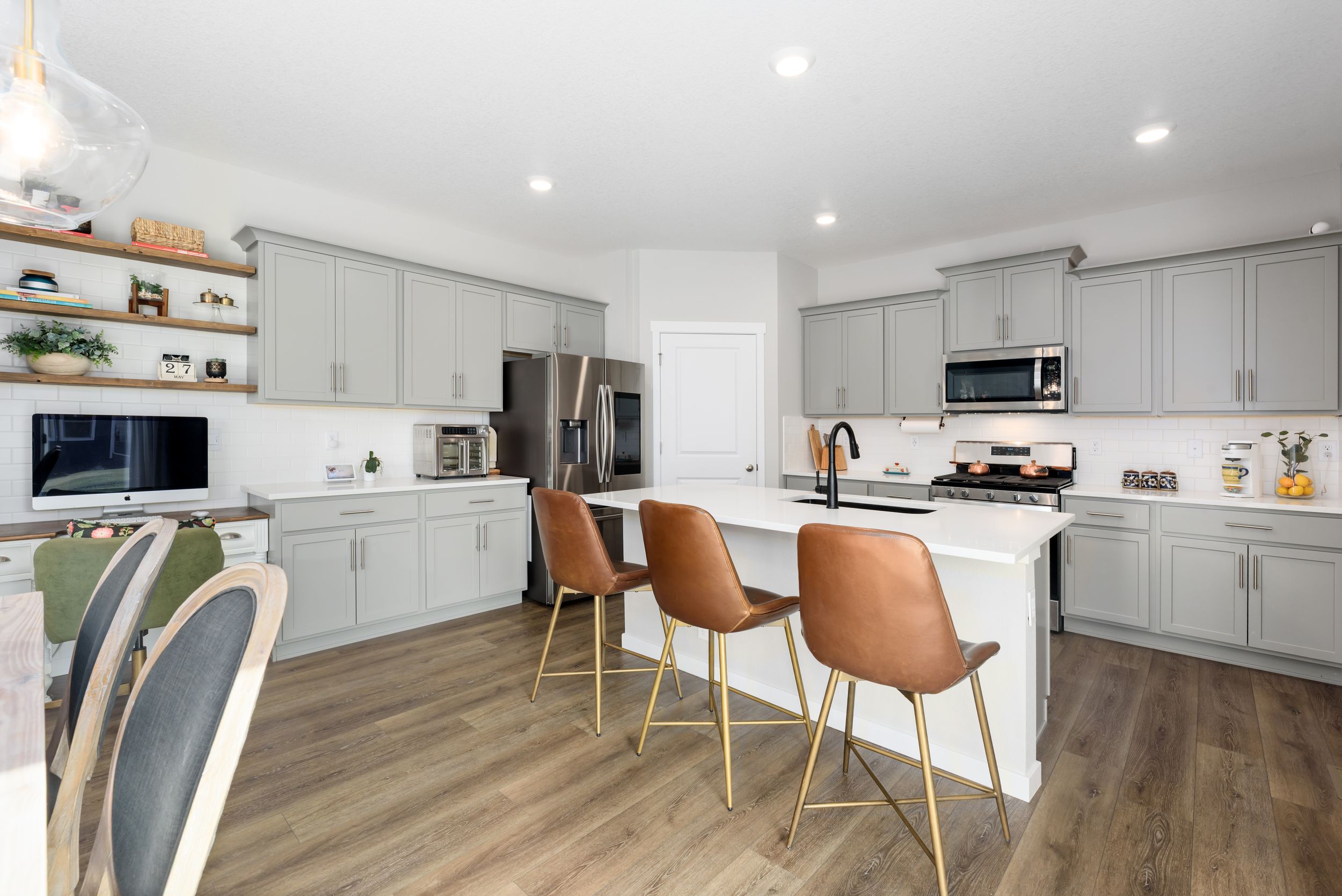 Modern white kitchen with hardwood floors, recessed lighting, and brown leather bar stools at a sleek breakfast counter.