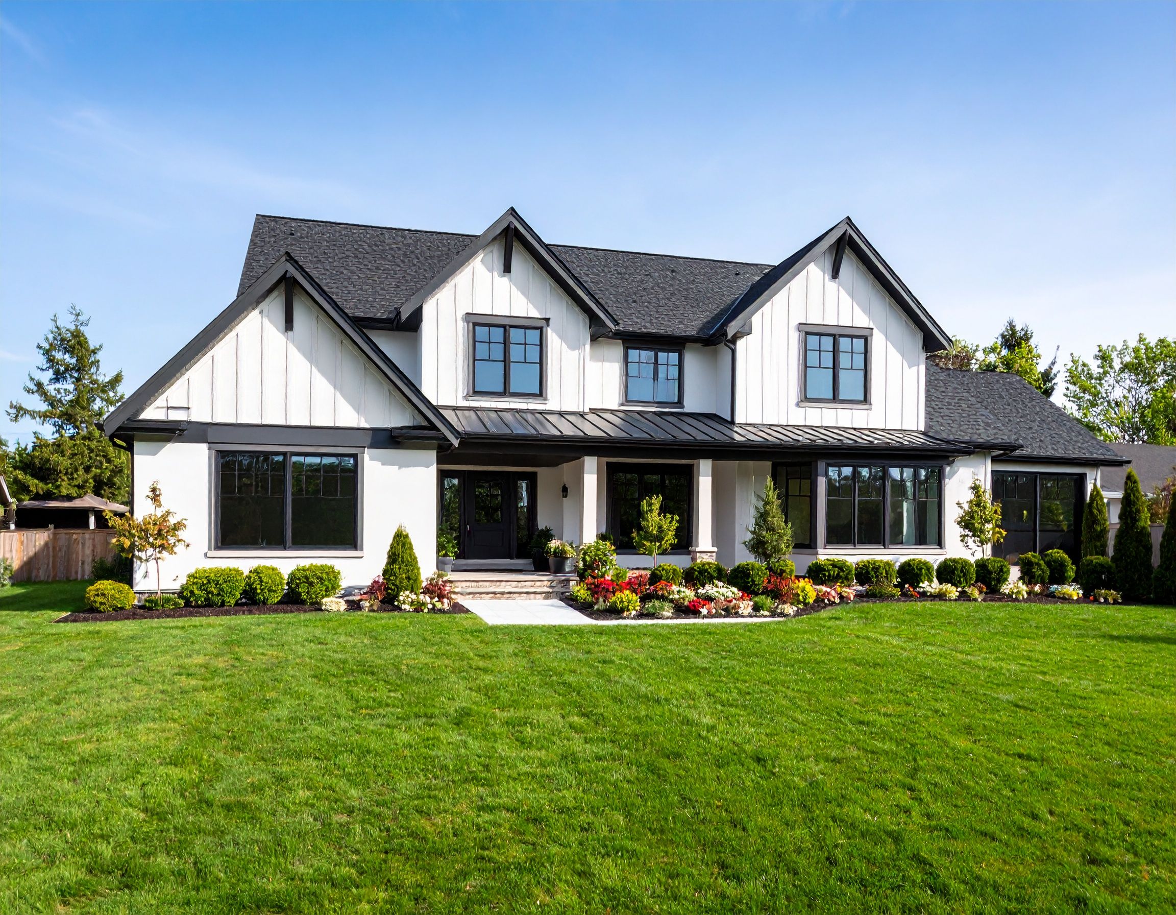 Modern farmhouse style home with white and black exterior, manicured lawn, and professional landscaping in front.