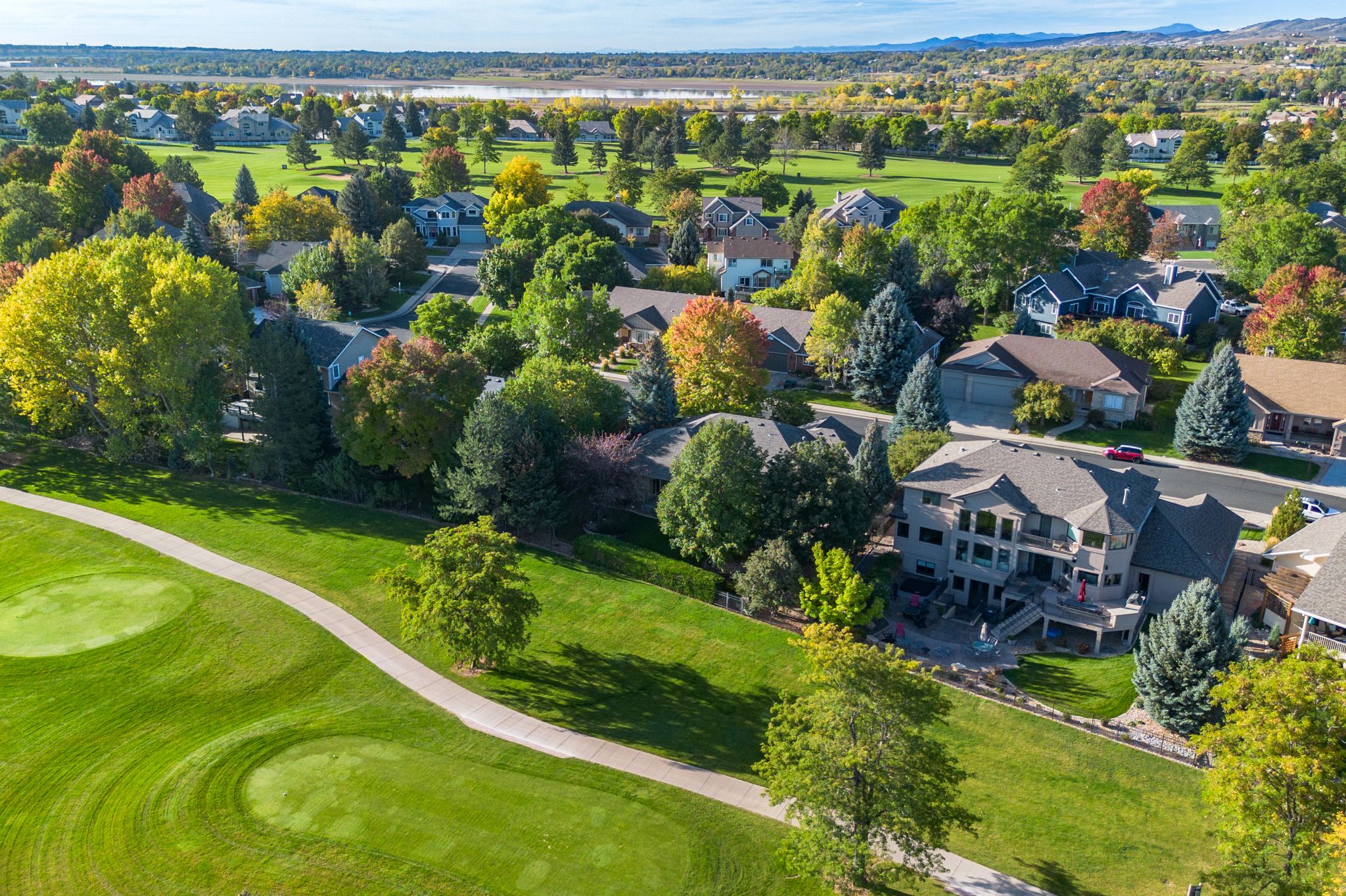 Aerial panoramic view of a golf course with green fairways, trees, and residential homes along the perimeter.