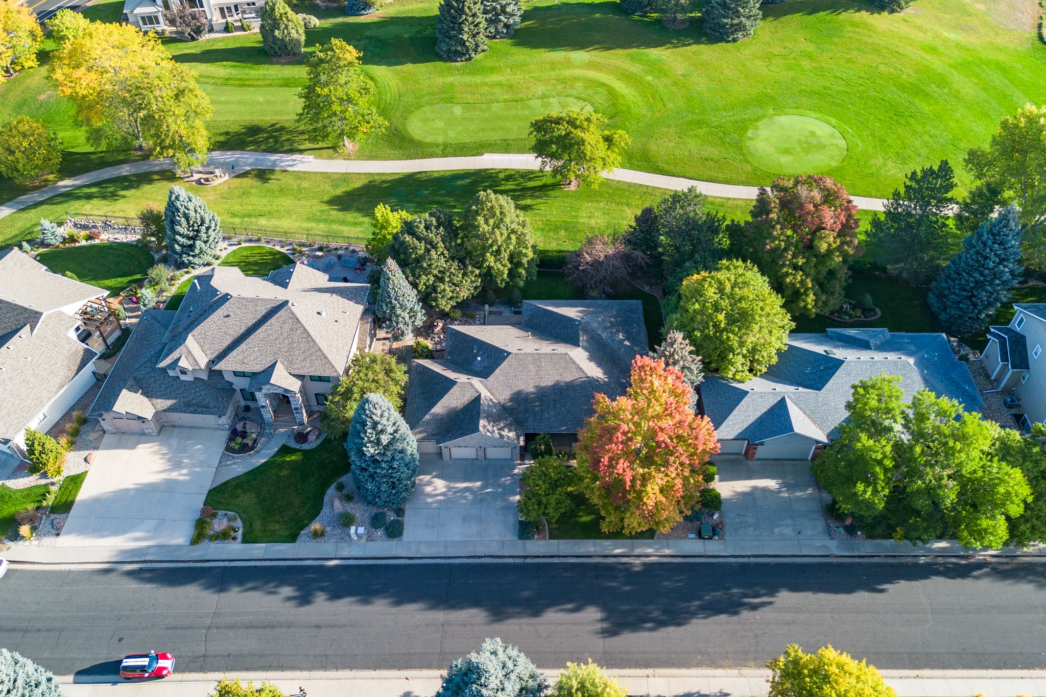 Aerial view of suburban homes with well-maintained green lawns and trees in a residential neighborhood on a sunny day.