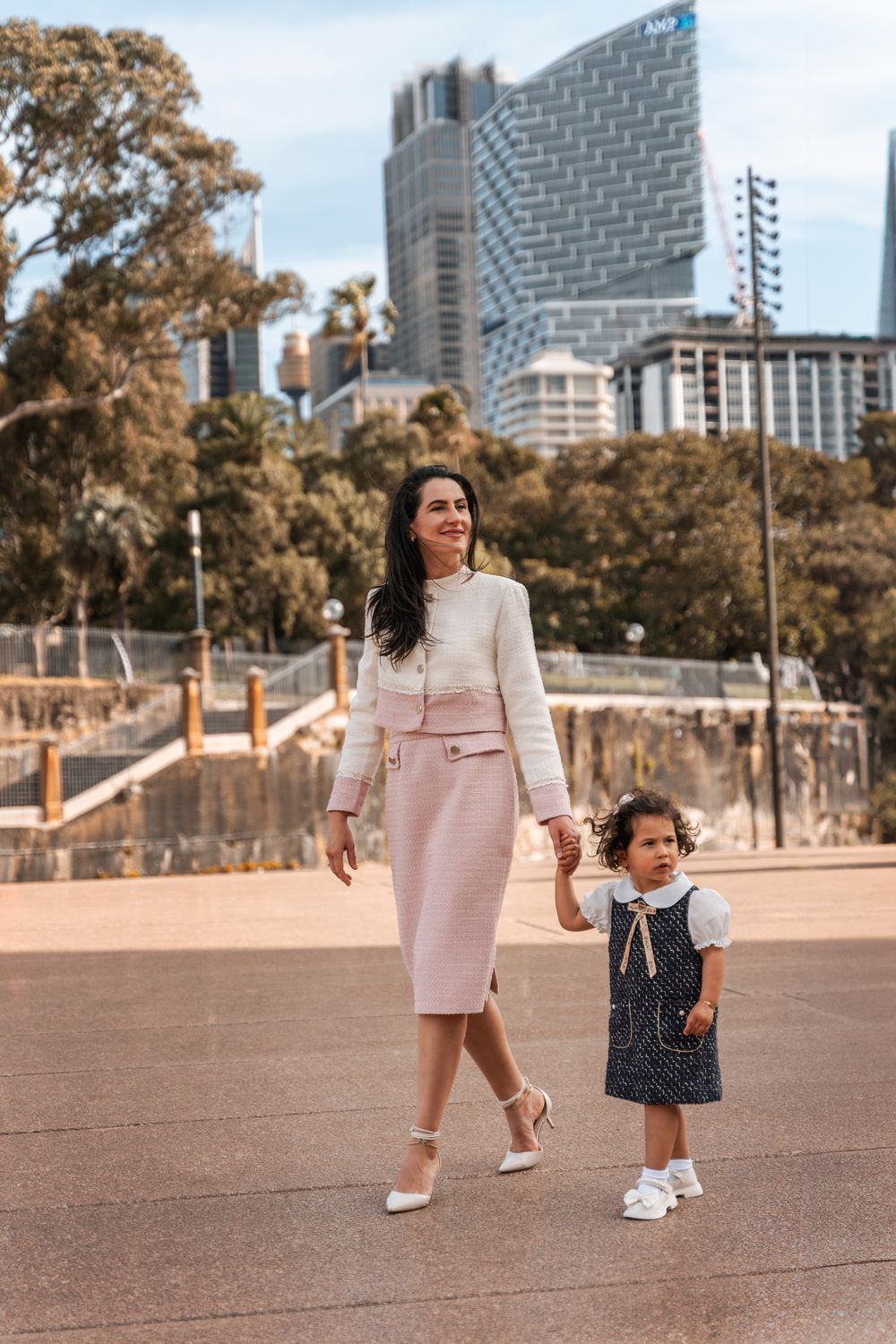 Elegant mother and daughter walking hand in hand in Sydney CBD, wearing matching pink and navy outfits.
