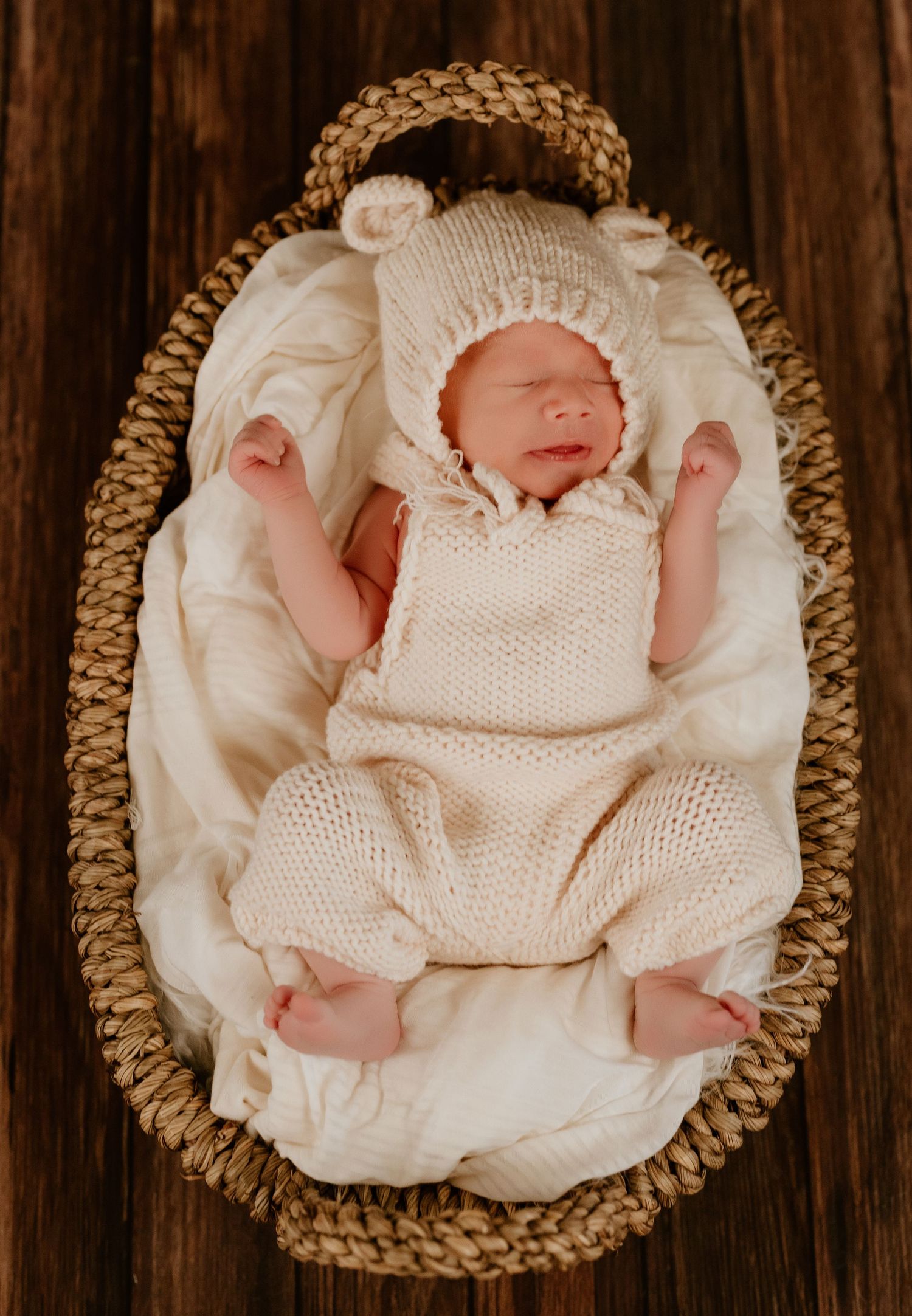 Newborn baby sleeping peacefully in white swaddle with brown bear hat.