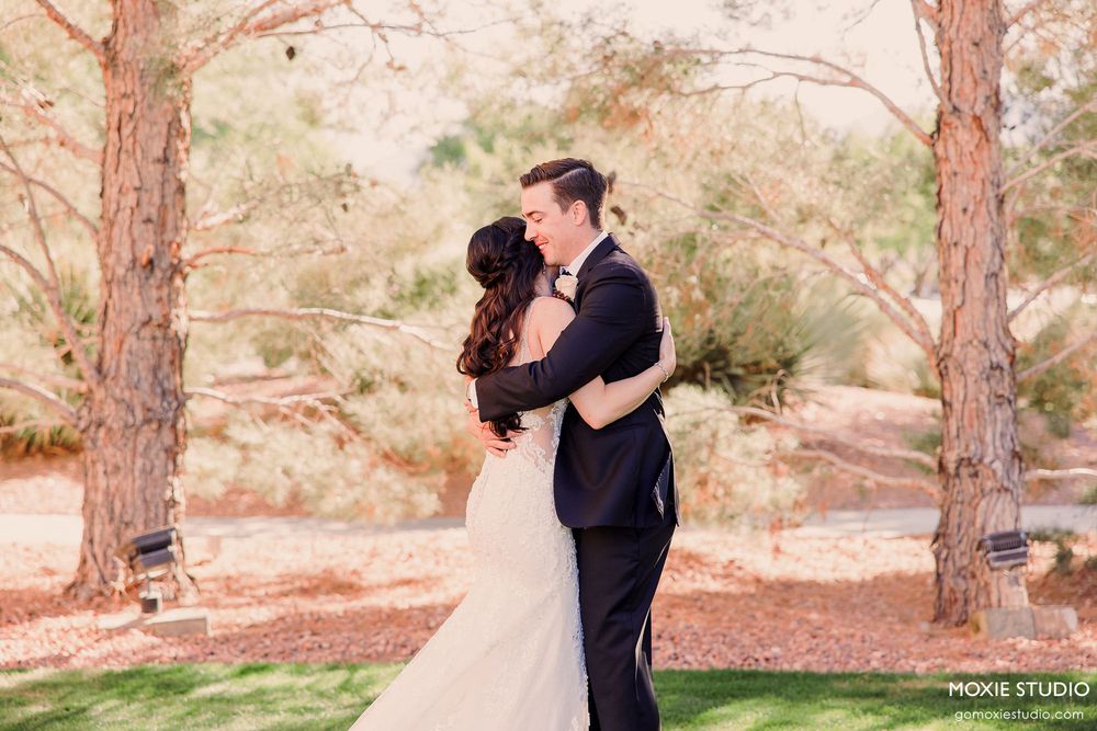Couple embraces in romantic outdoor wedding photoshoot among tall pine trees in natural desert setting.
