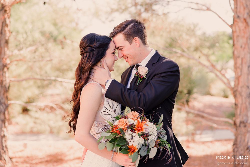Newlyweds share intimate moment in rustic outdoor setting with desert landscape and pine trees.