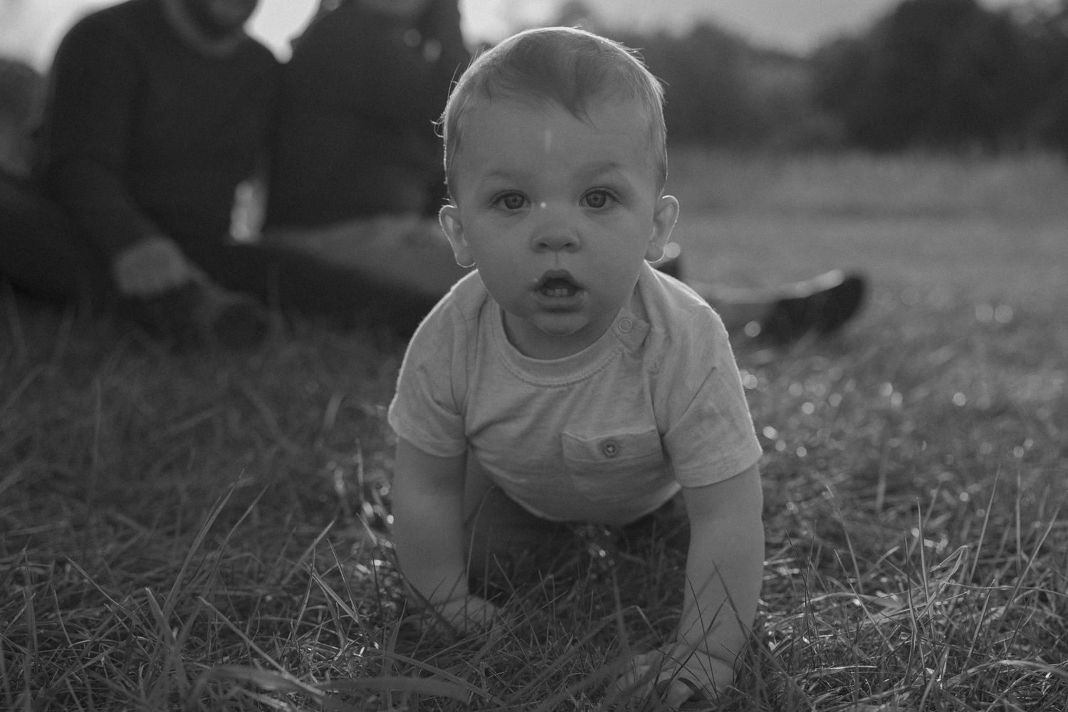 A black and white photo of a baby crawling on grass outdoors.