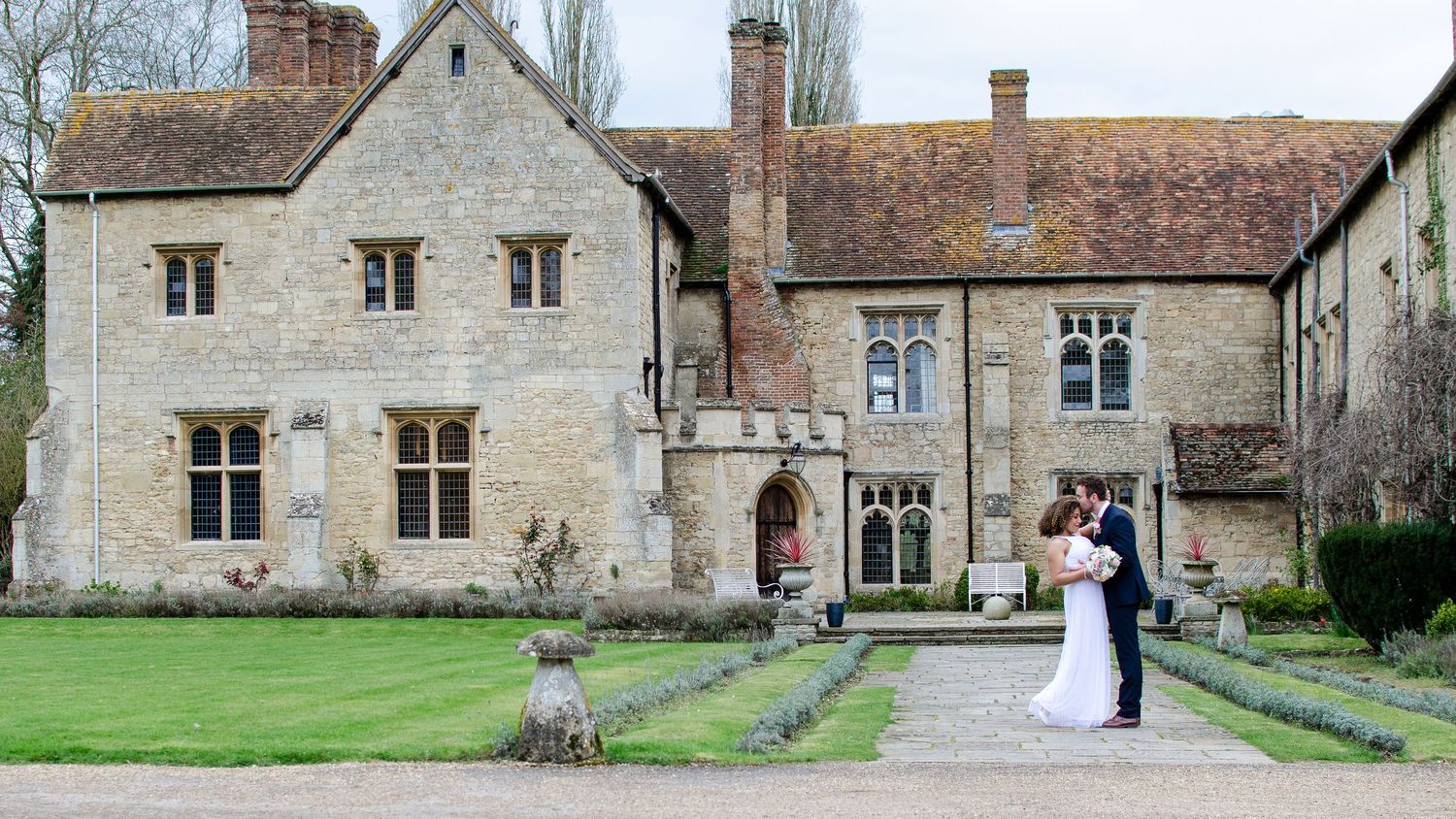 Wedding couple standing together in front of a grand historic English manor house.