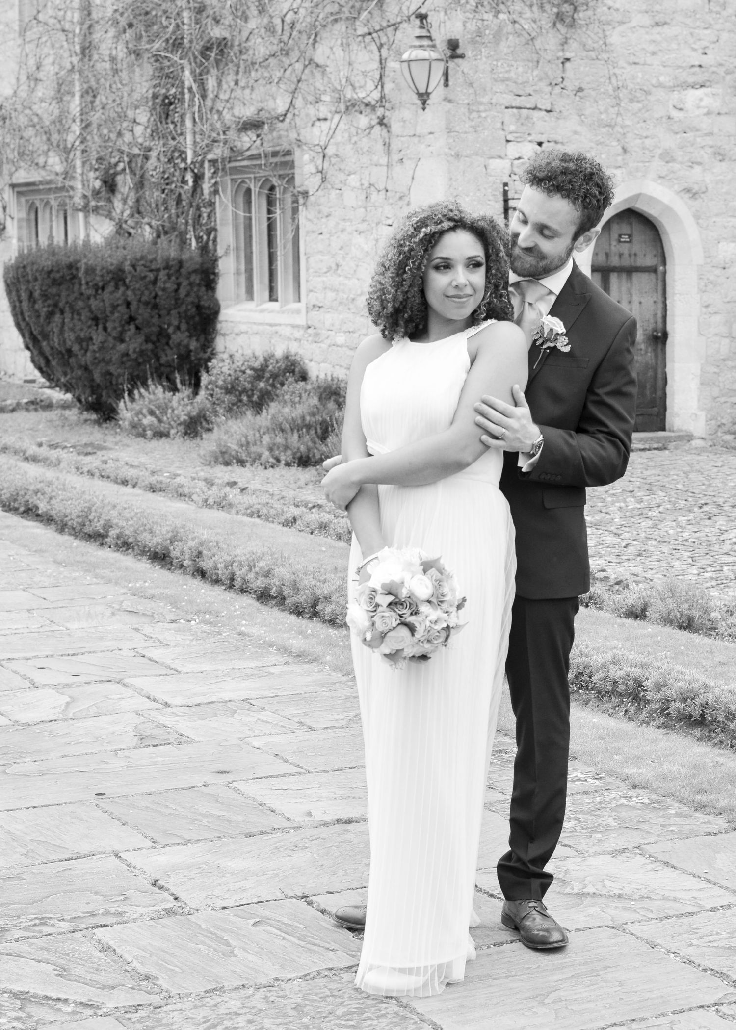 Black and white wedding portrait of couple embracing outside a stone manor house.