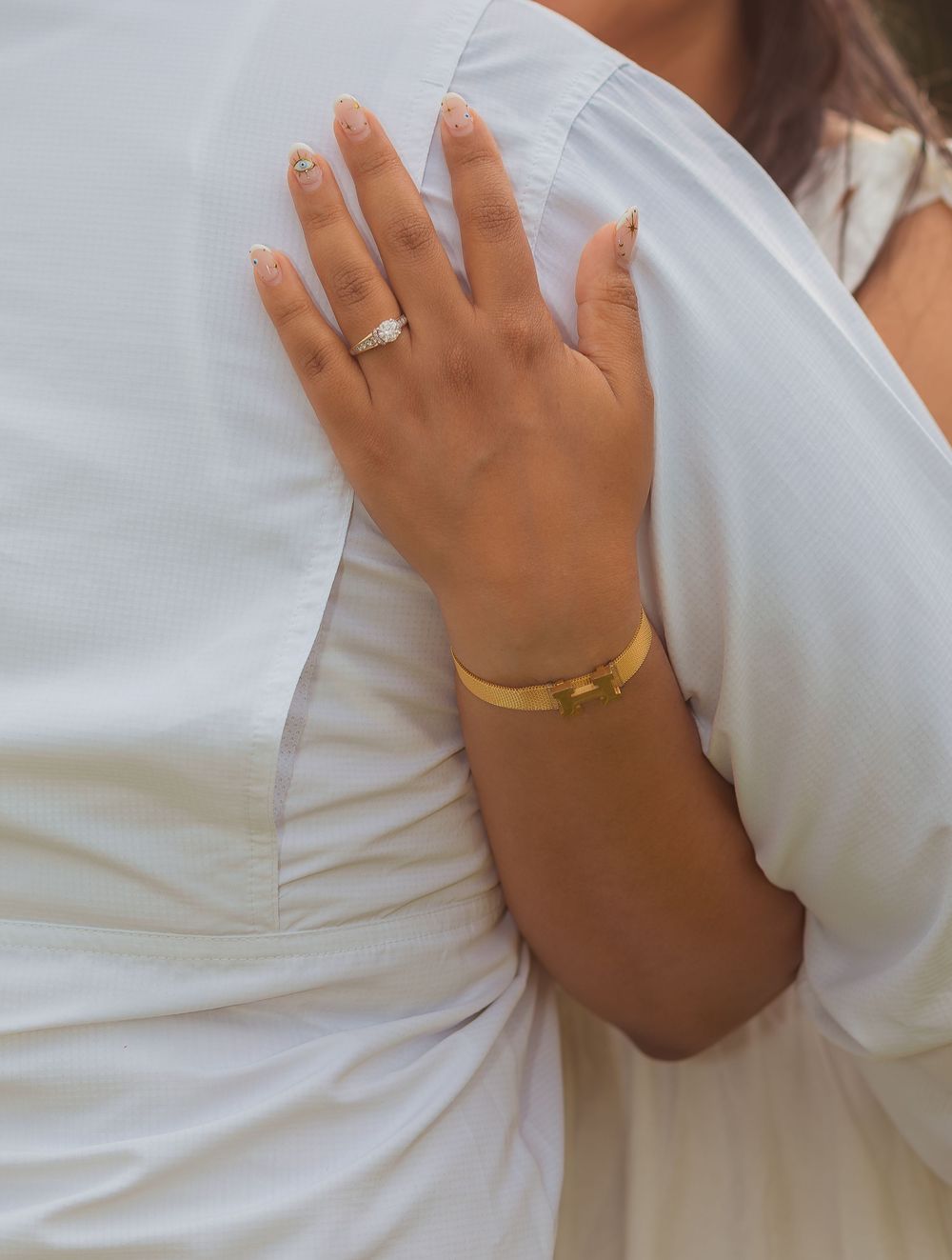Close-up detail of hands wearing gold and silver rings against a white dress fabric background.