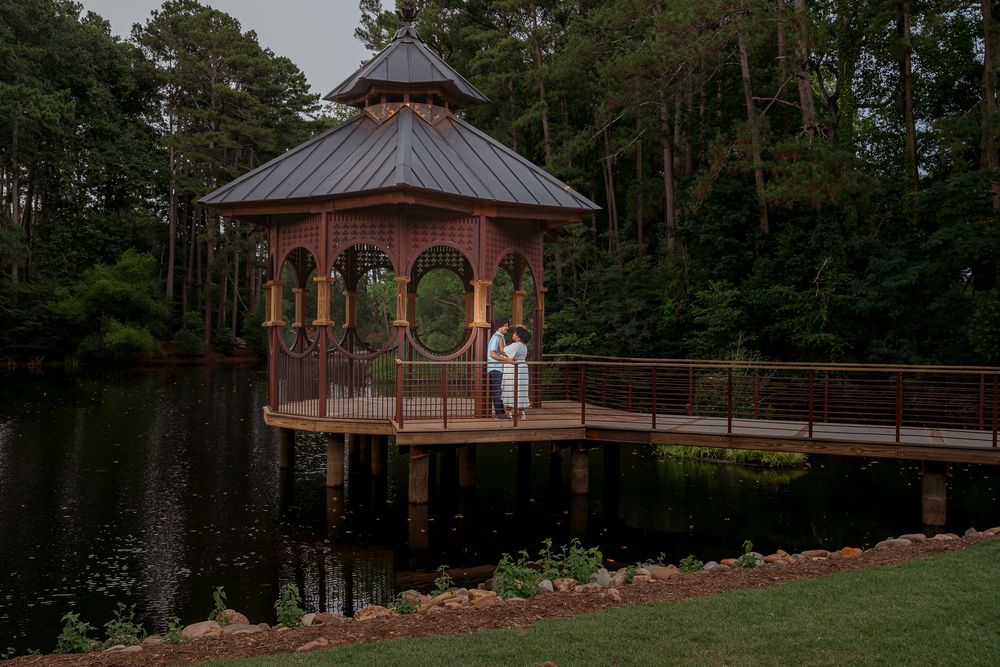 A series of wooden gazebos with copper roofs connected by a winding pathway in a wooded park setting.