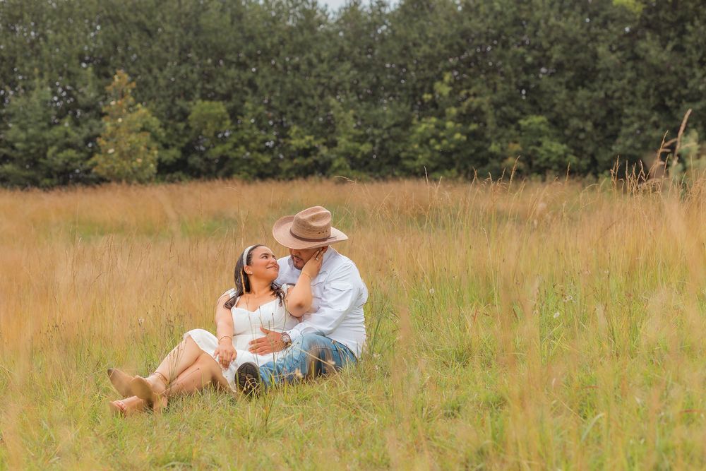 A couple enjoys a romantic picnic together in a sunlit meadow with tall golden grass and trees in the background.