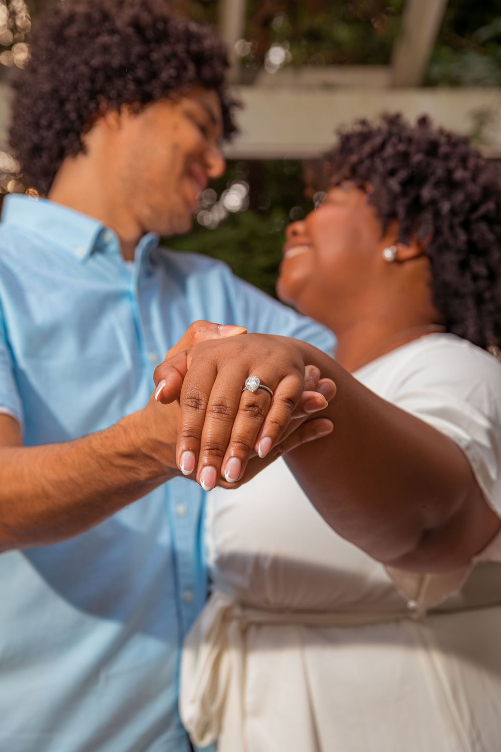 A joyful couple holding hands and laughing together outdoors, with one wearing blue and the other in white.