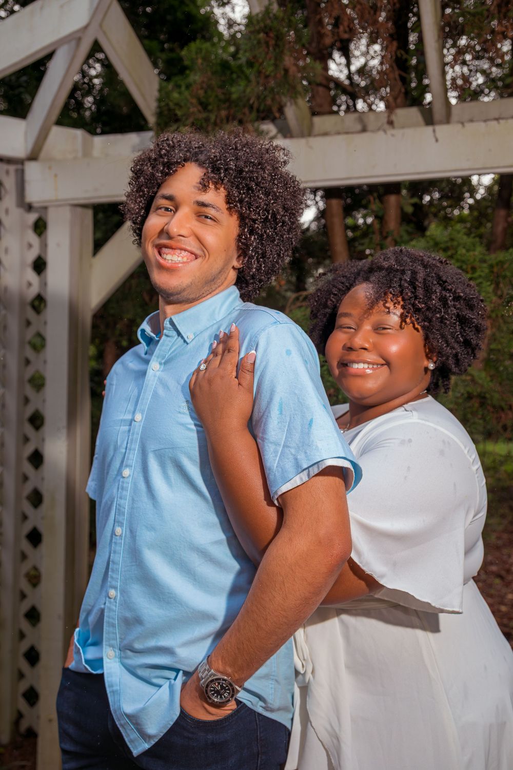 Two people in casual attire share a joyful moment together outdoors near a white pergola structure.