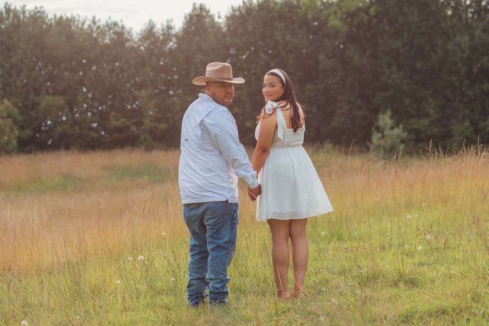 A couple stands together in a sunlit meadow during golden hour, creating a romantic silhouette against the tall grass.