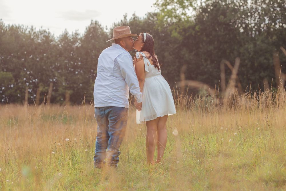 A couple walks through a sunlit meadow at golden hour holding hands and sharing a romantic moment together.
