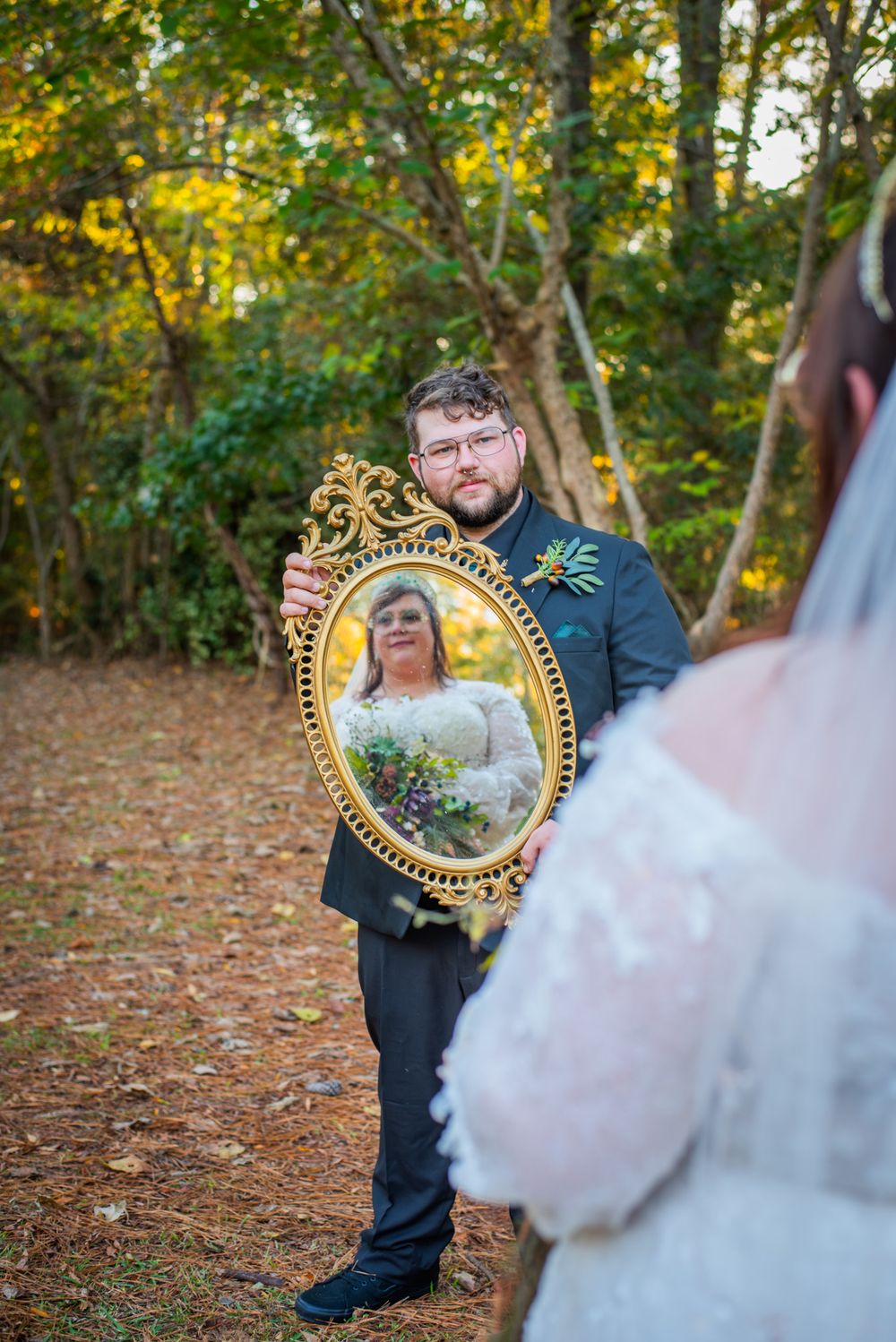 A creative wedding photo showing someone holding an mirror in a wooded setting.