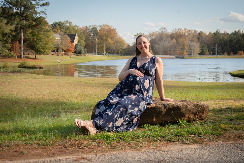 A woman in a floral dress poses gracefully on a log by a serene lake during autumn.
