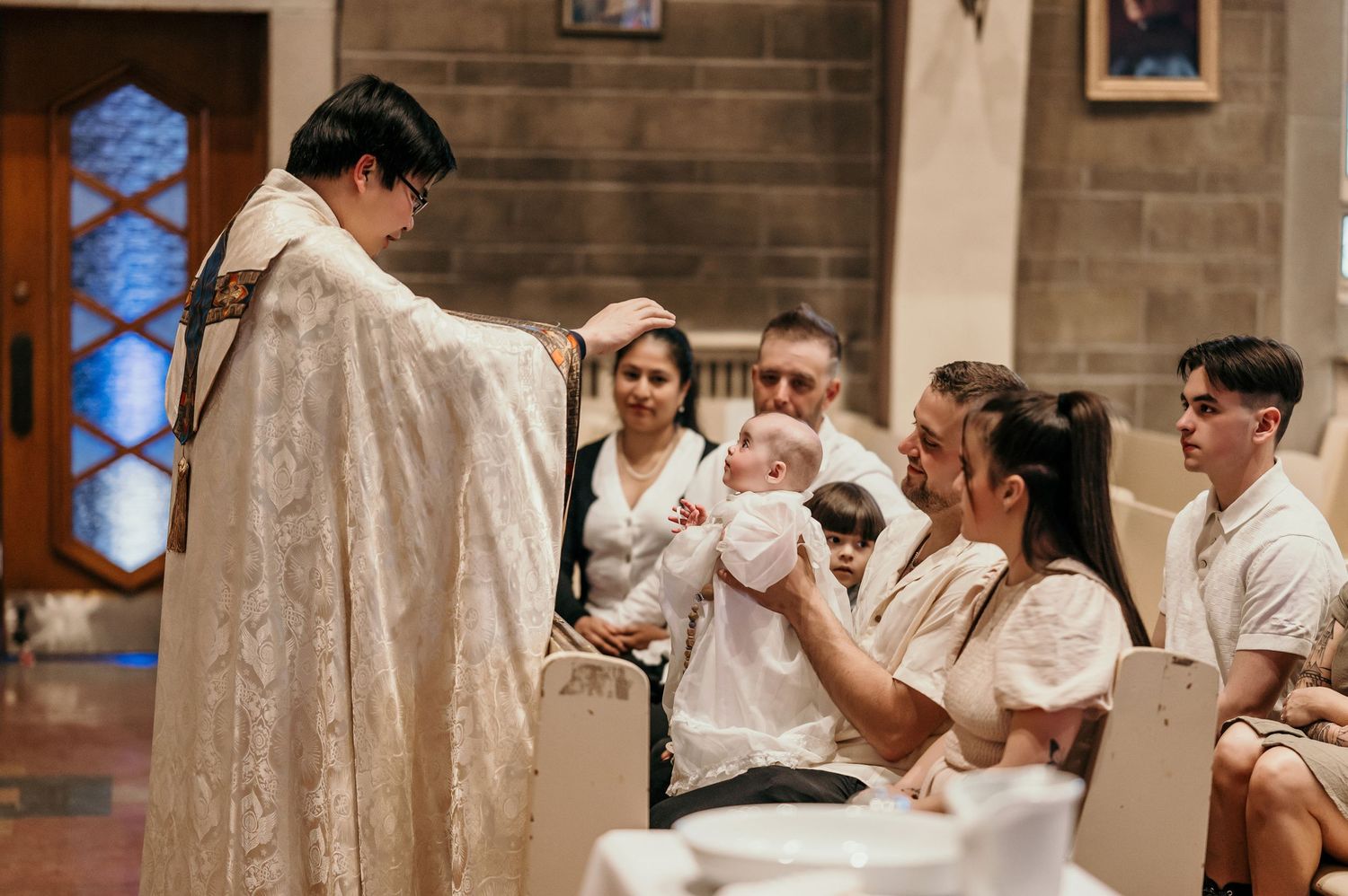 A religious baptism ceremony takes place in a church as family members gather around to witness the sacred moment.