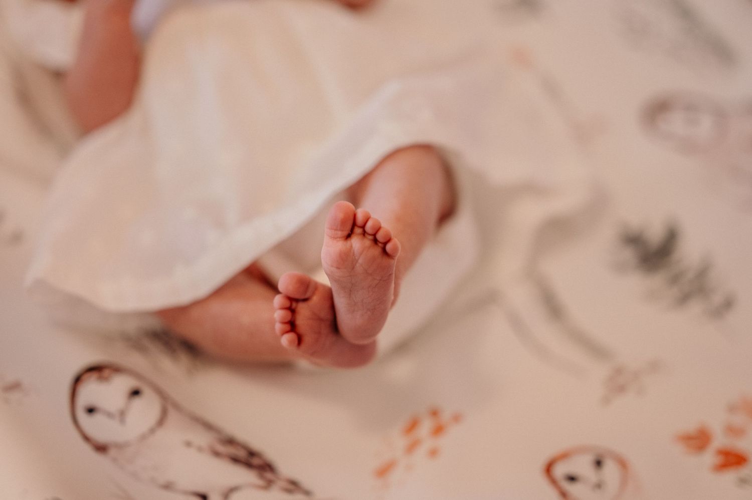 Tiny newborn baby feet with hospital identification tags and blanket in soft pink tones.