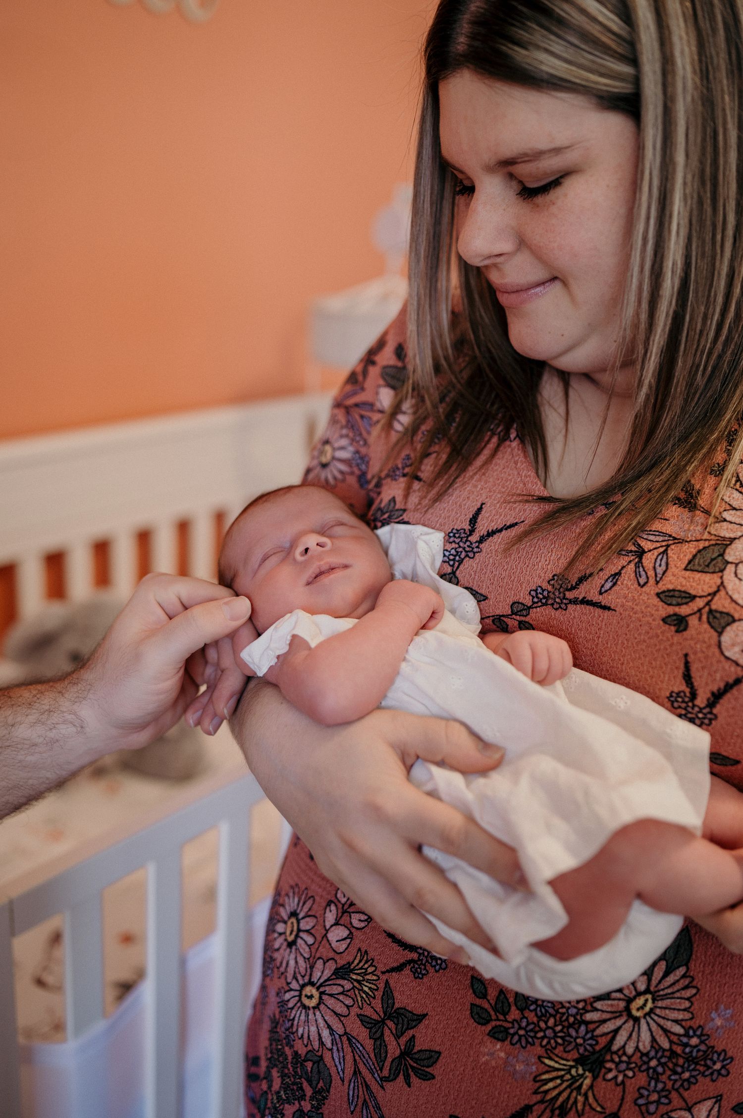 A mother in a floral dress holds and gazes lovingly at her newborn baby wrapped in a white blanket.