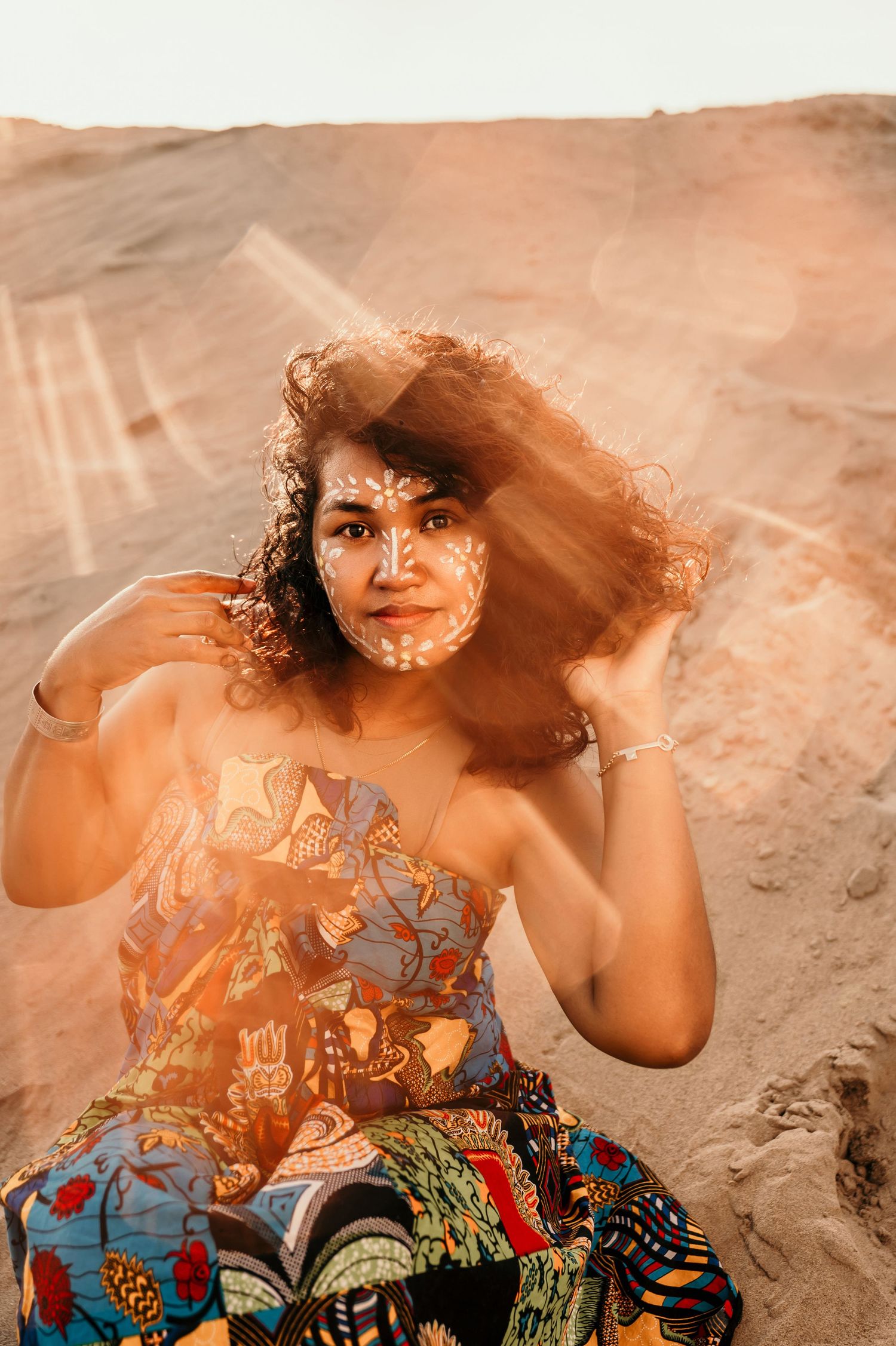 A person in a floral dress poses on a sandy beach with flowing hair in a warm sepia-toned photo series.
