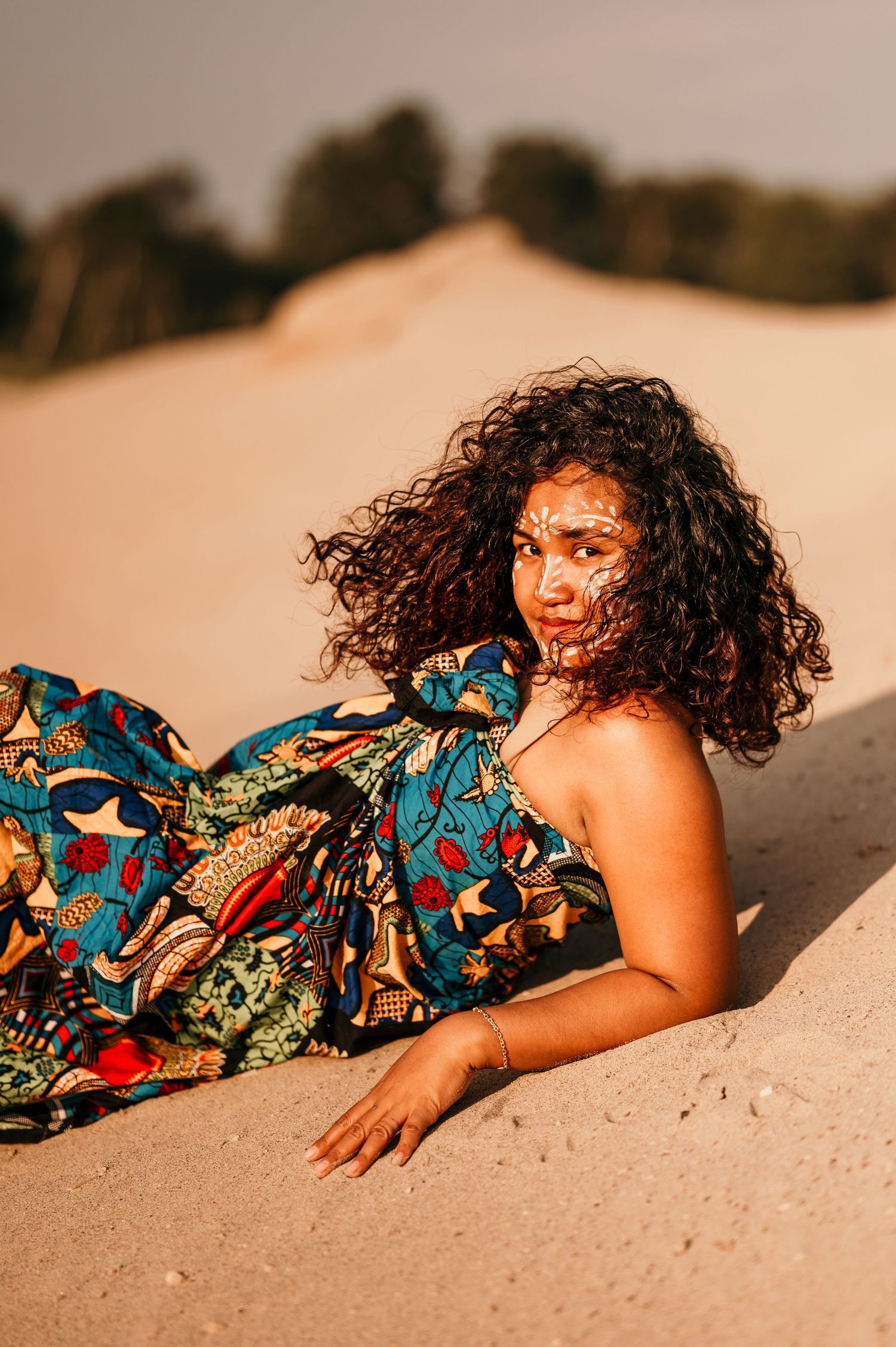 Person in colorful patterned dress lying on sandy beach at sunset creating artistic portrait series.