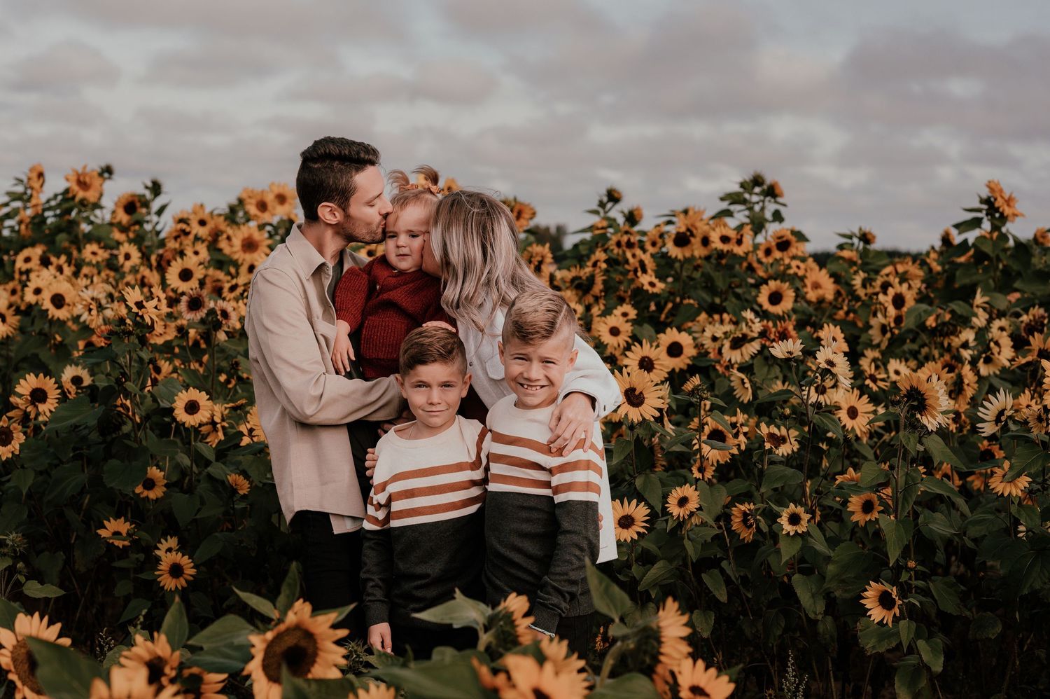 A family embraces in a blooming sunflower field during golden hour.
