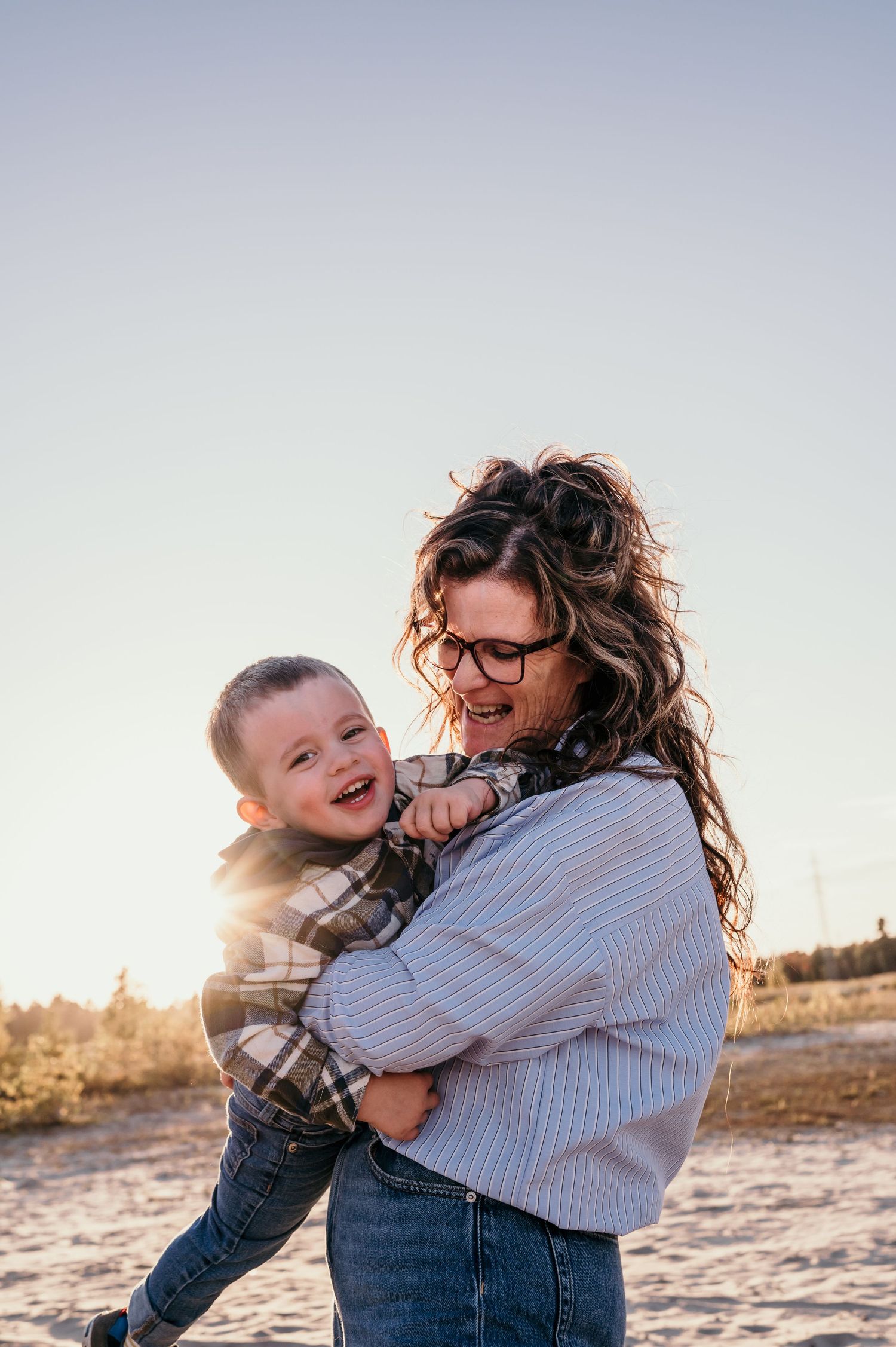 A joyful embrace between parent and child laughing together at sunset on a sandy beach.