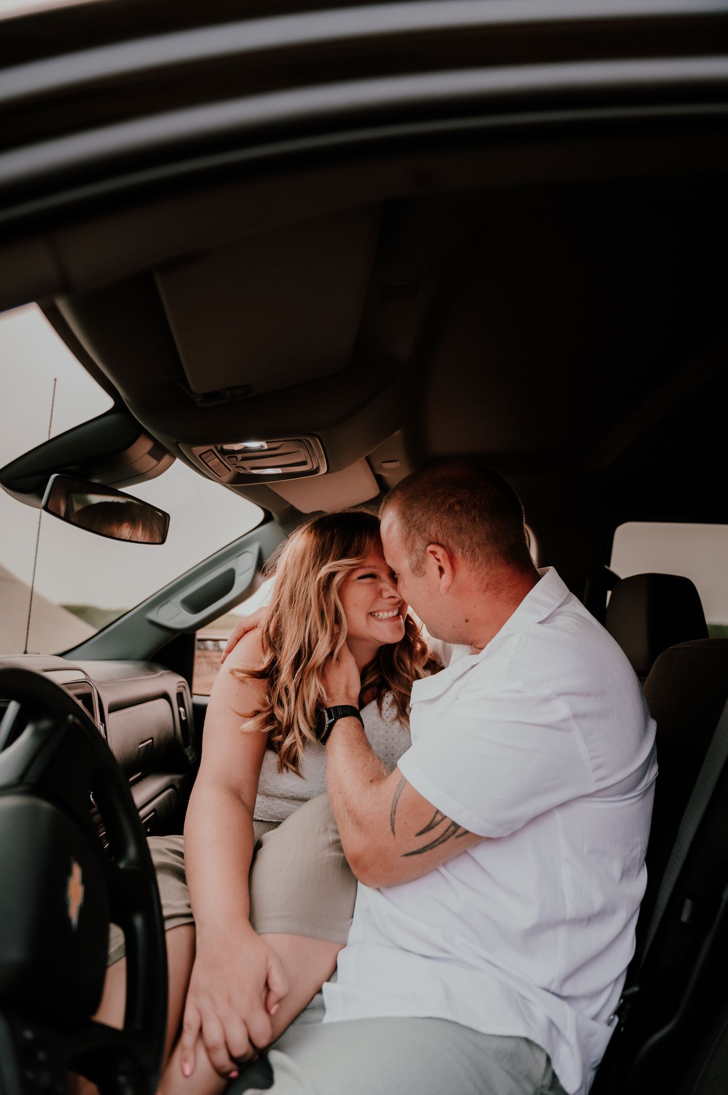 A couple shares an intimate moment in the front seat of a car during a romantic photoshoot.