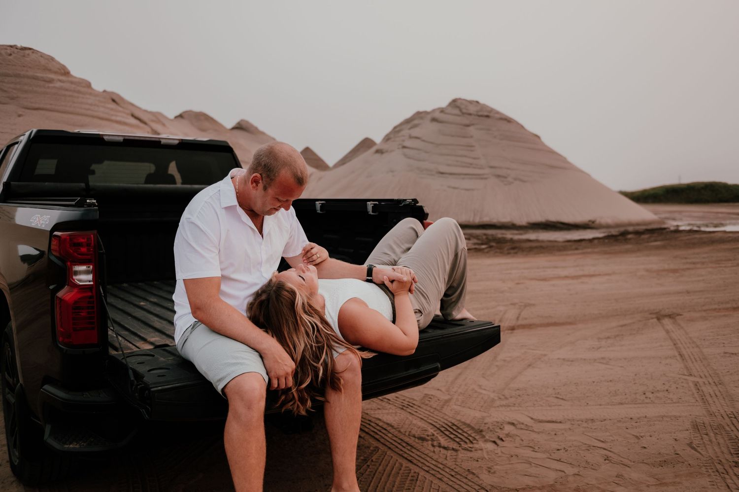 A couple sits together on the tailgate of a truck in a desert landscape.