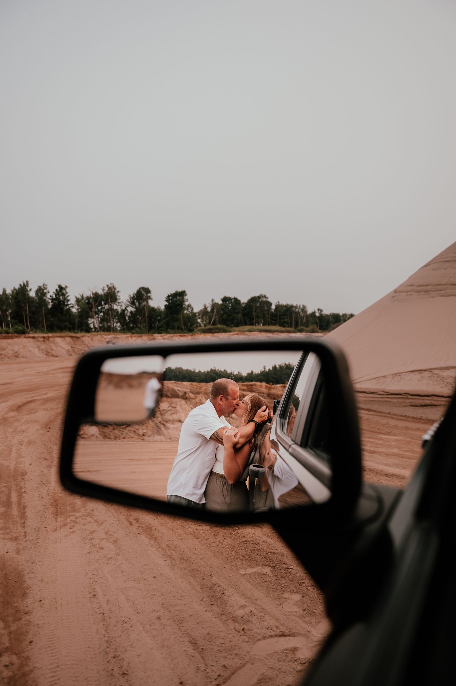 A rearview mirror reflection captures a couple's tender moment on a desert road.