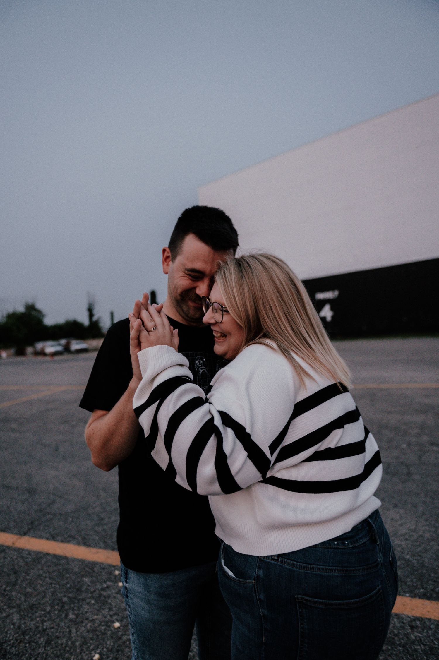 Intimate couples portrait sharing a laugh in an empty parking lot at dusk.