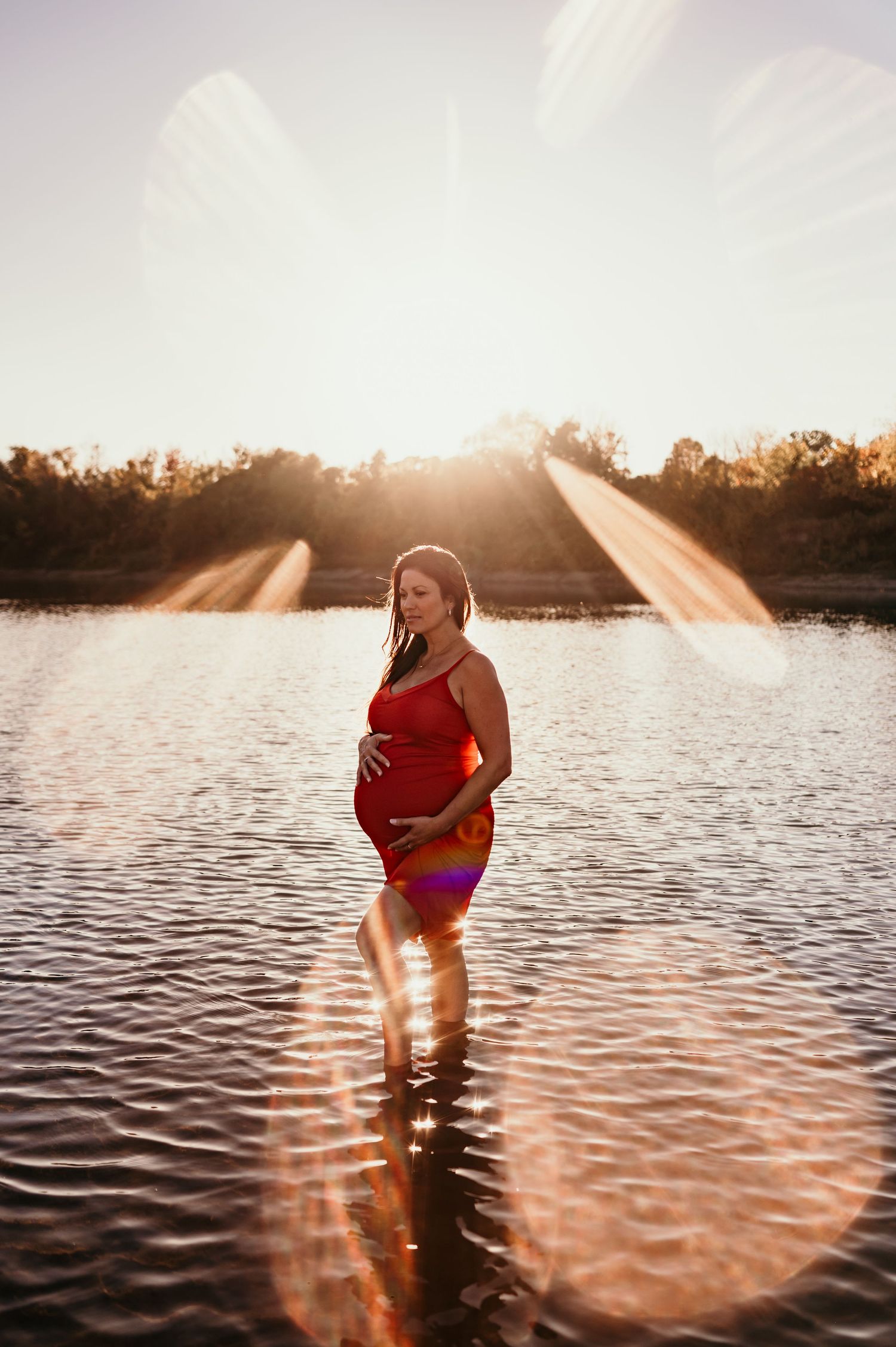 A silhouetted figure stands in calm lake waters during golden hour sunset creating a dreamy atmospheric scene.
