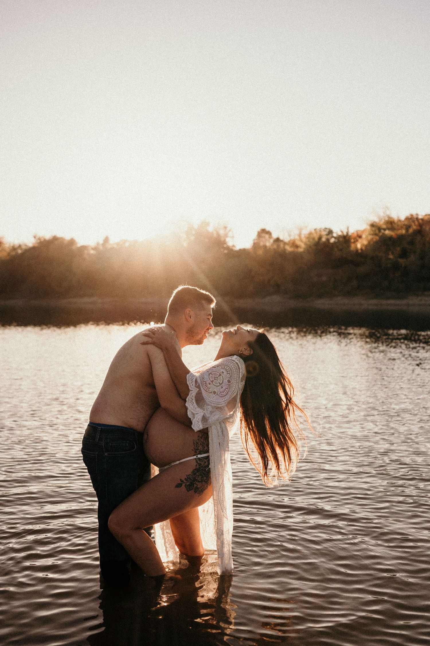Silhouetted couple embraces in a lake at sunset with golden light reflecting off the rippling water.