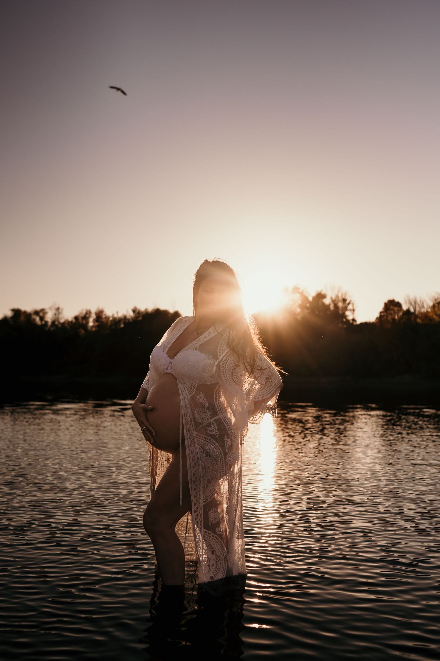 A silhouetted figure stands in a lake during sunset with sunlight creating a golden glow on the water.