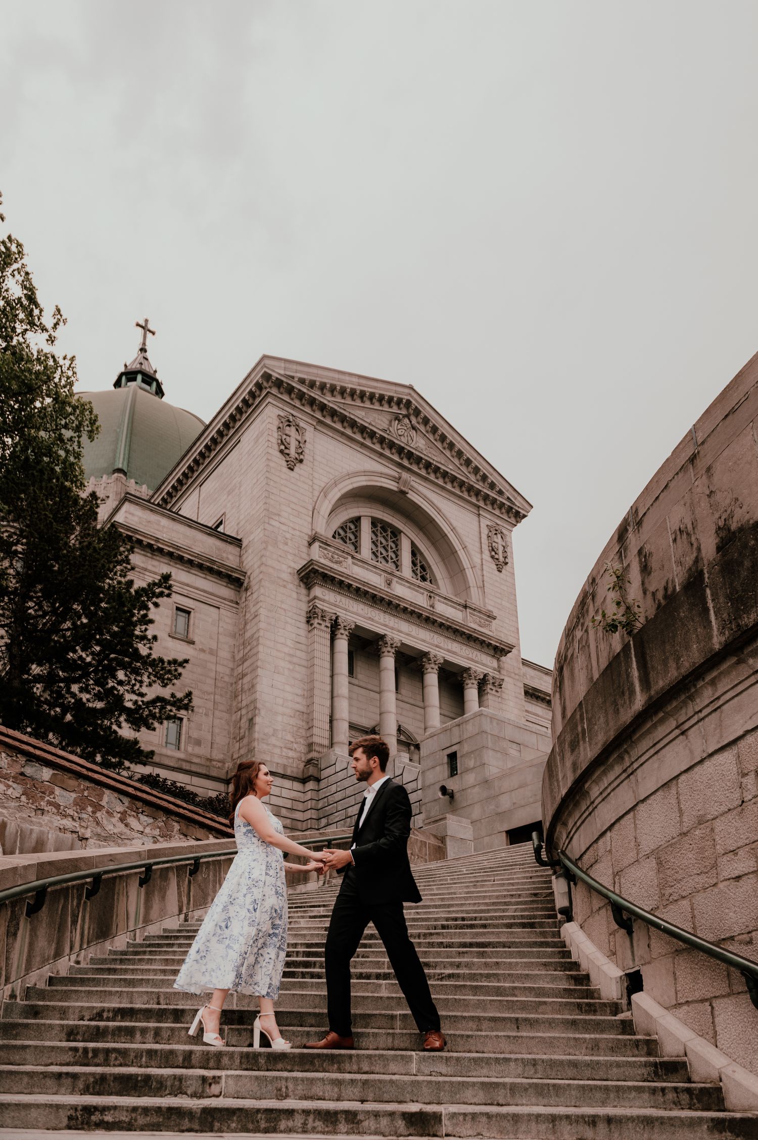 A couple stands on grand stone steps leading to a classical church building.