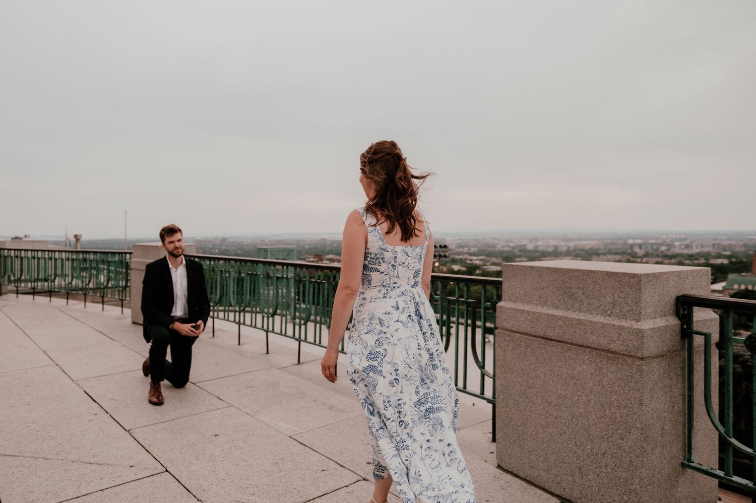 A couple walking on a rooftop terrace with city views, the woman wearing a flowing floral dress.