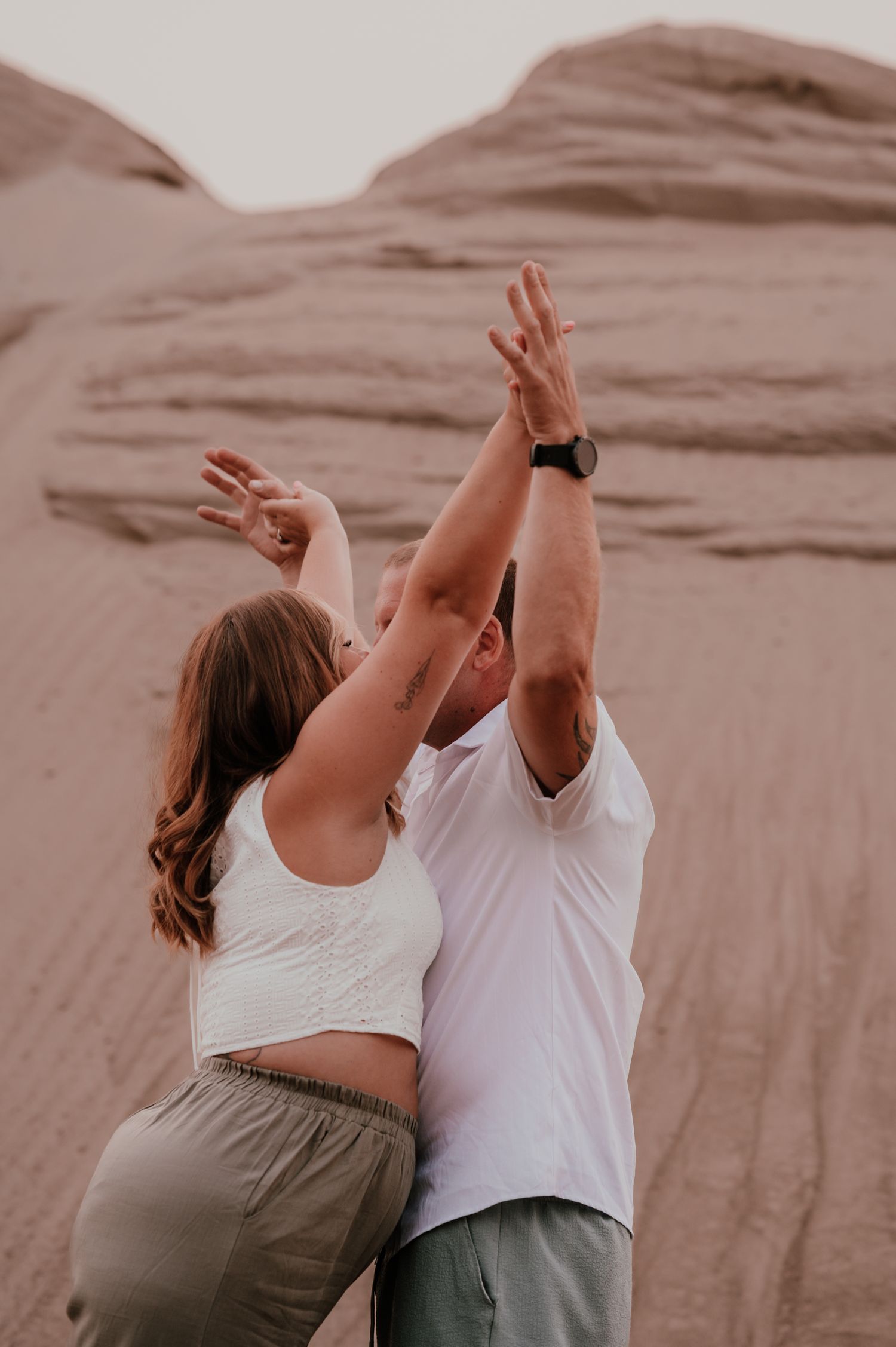 A couple raises their arms in celebration against sandy desert cliffs.
