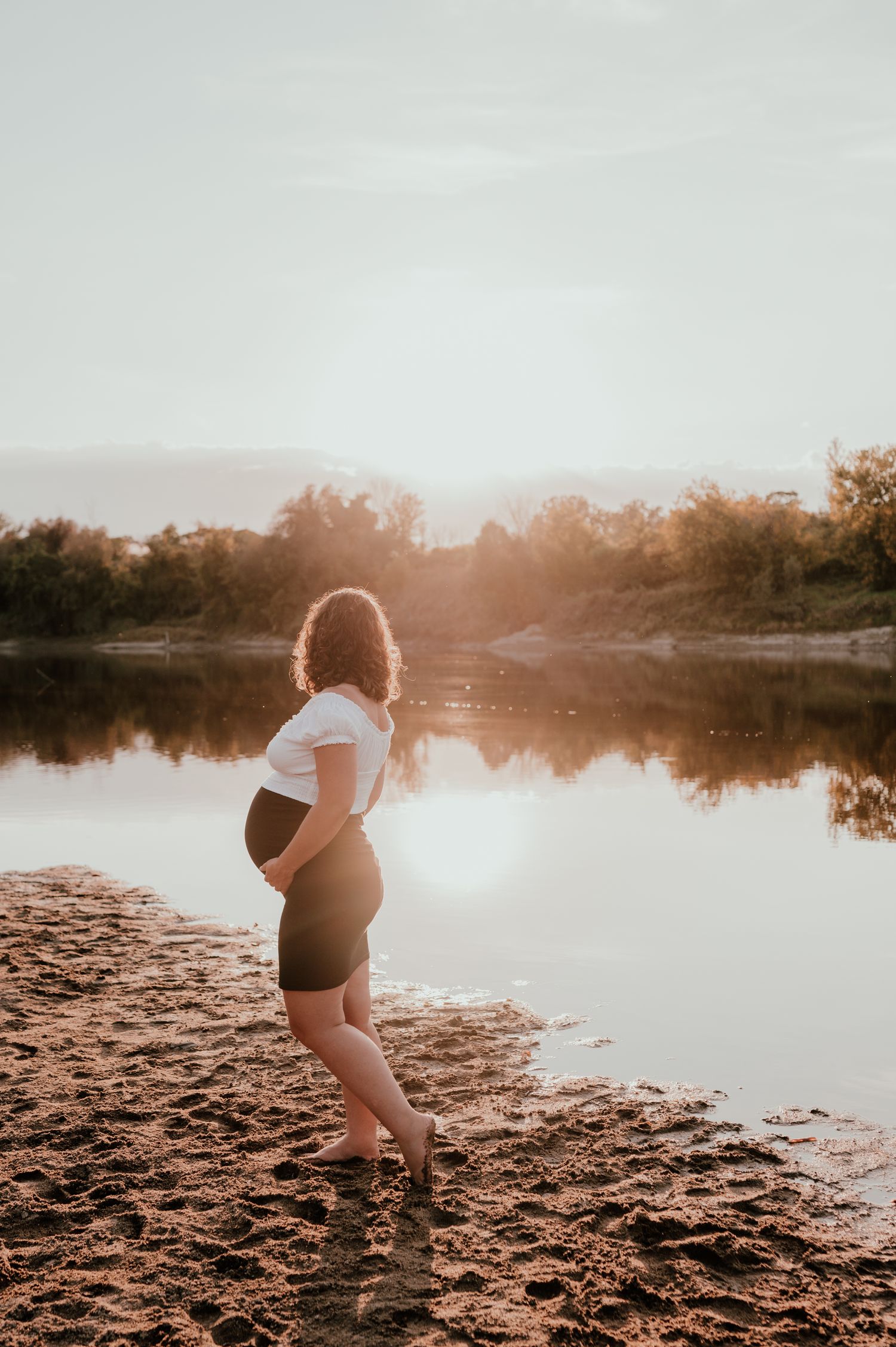 A person stands on a beach shoreline during golden hour with water reflections.
