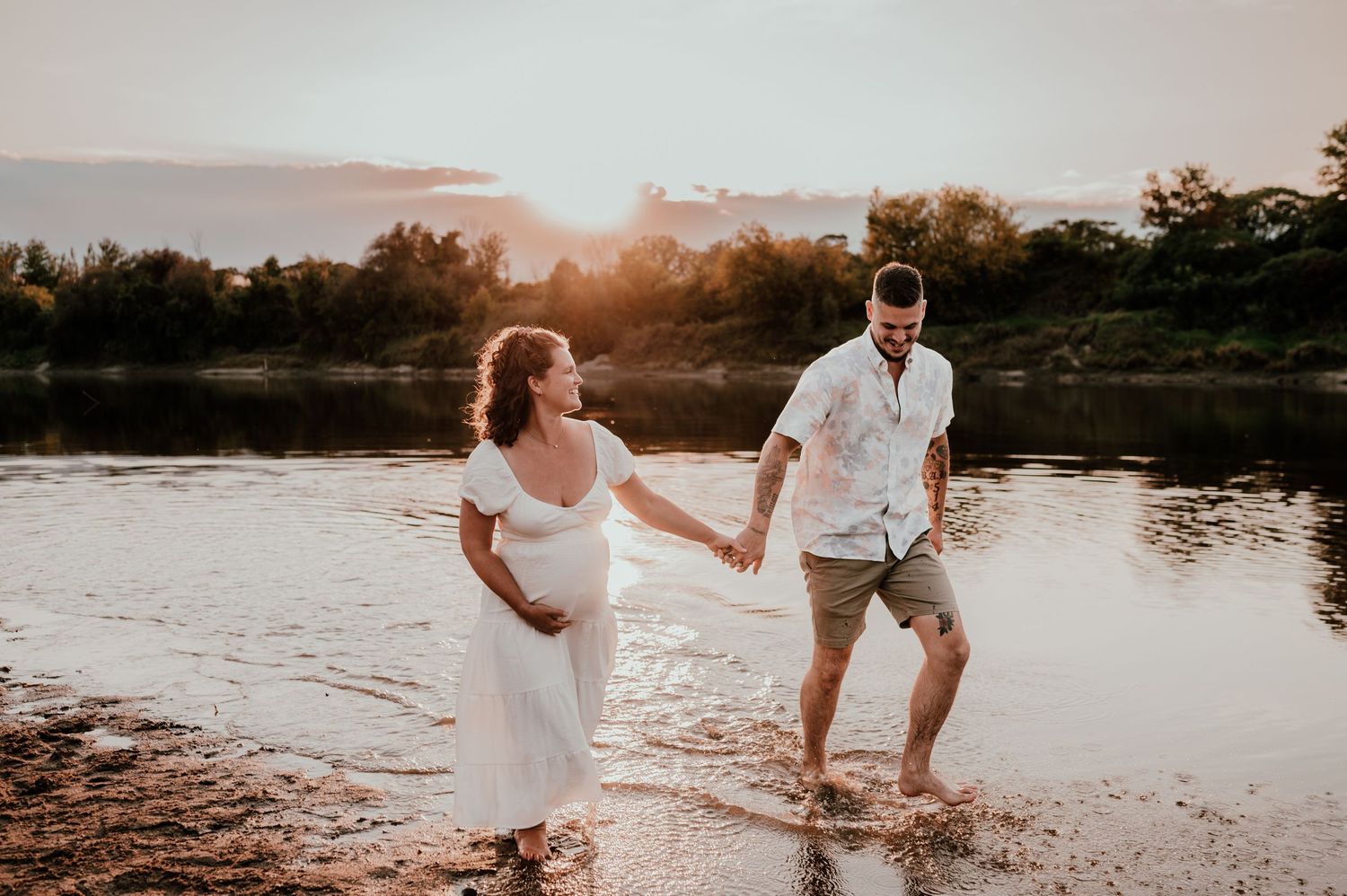 A couple splashes and plays in shallow river water during a golden sunset.