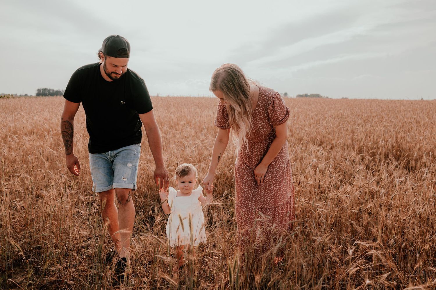 A family walks together through a golden wheat field at sunset.