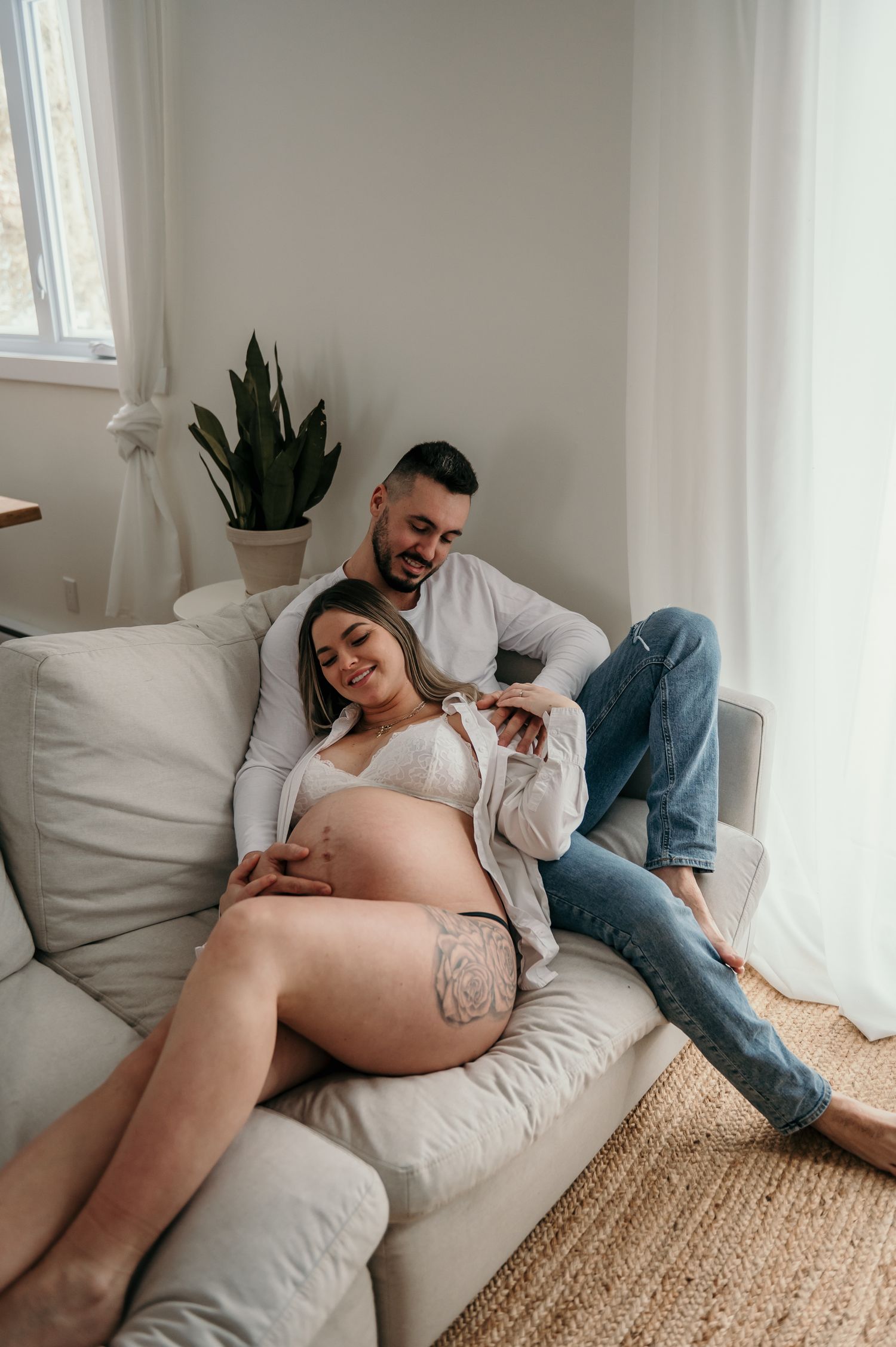 Couple relaxing together on light gray couch near window with natural lighting and jute rug.