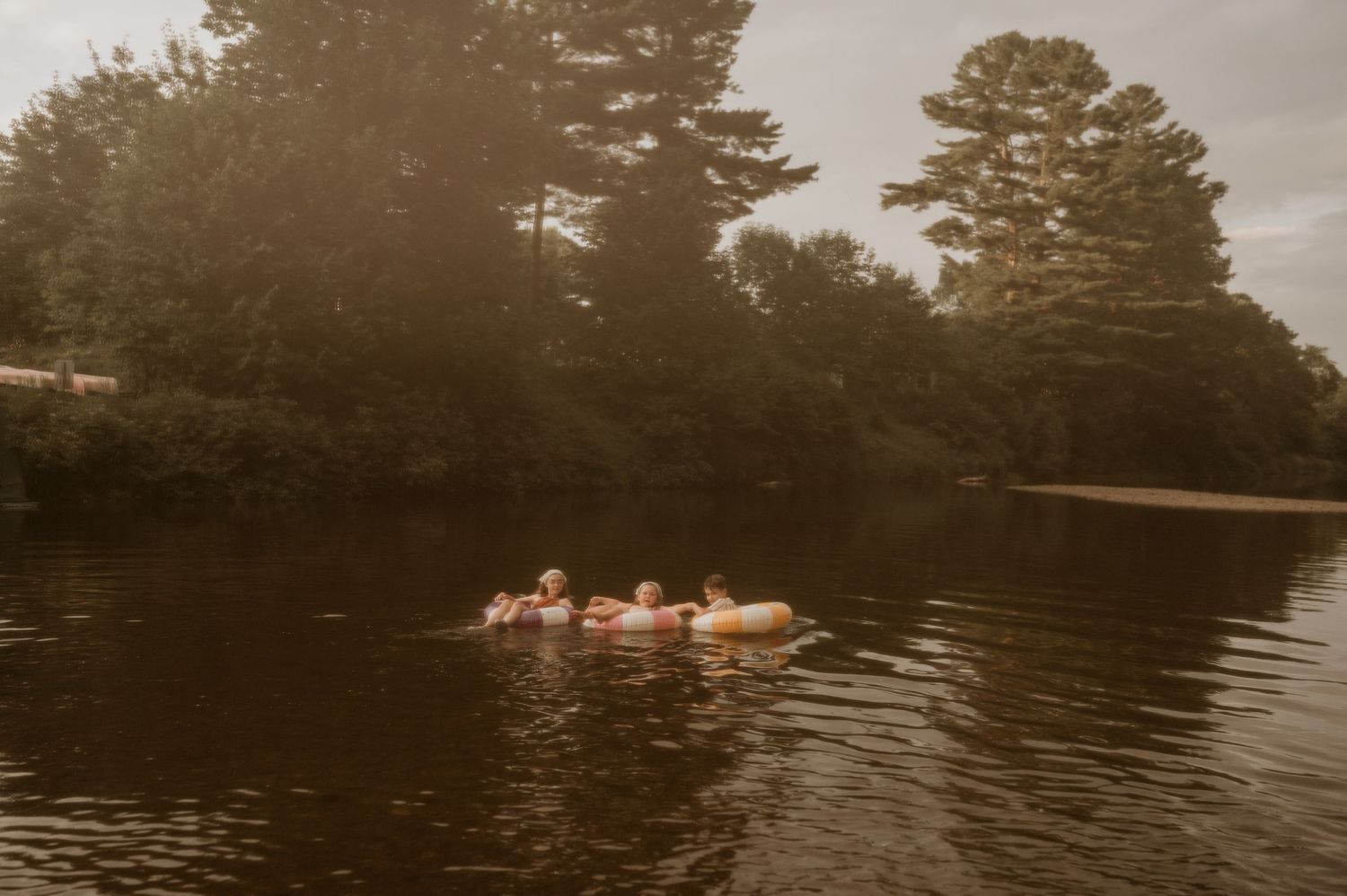 Group of people floating on inner tubes on a calm river surrounded by lush green trees on a misty day.