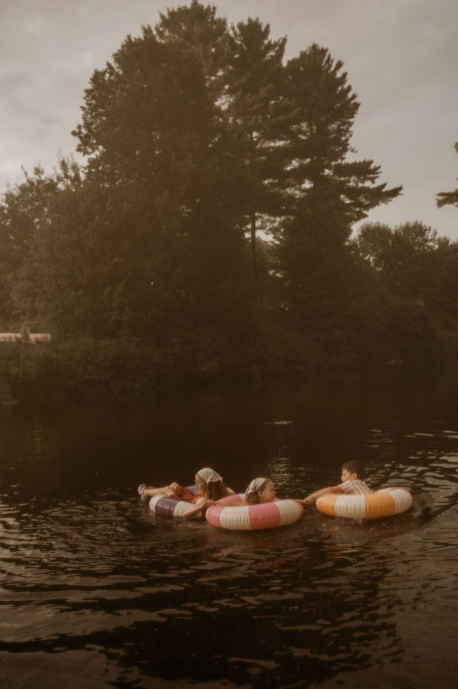 People floating on colorful striped inner tubes on a calm river surrounded by lush green trees.