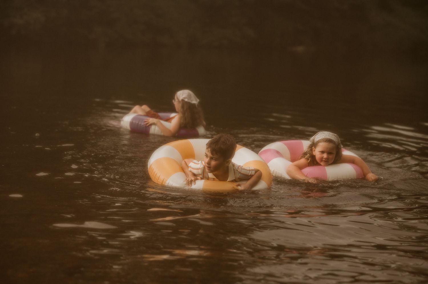 Children floating on colorful inflatable rings in a calm river during a sunny summer day.