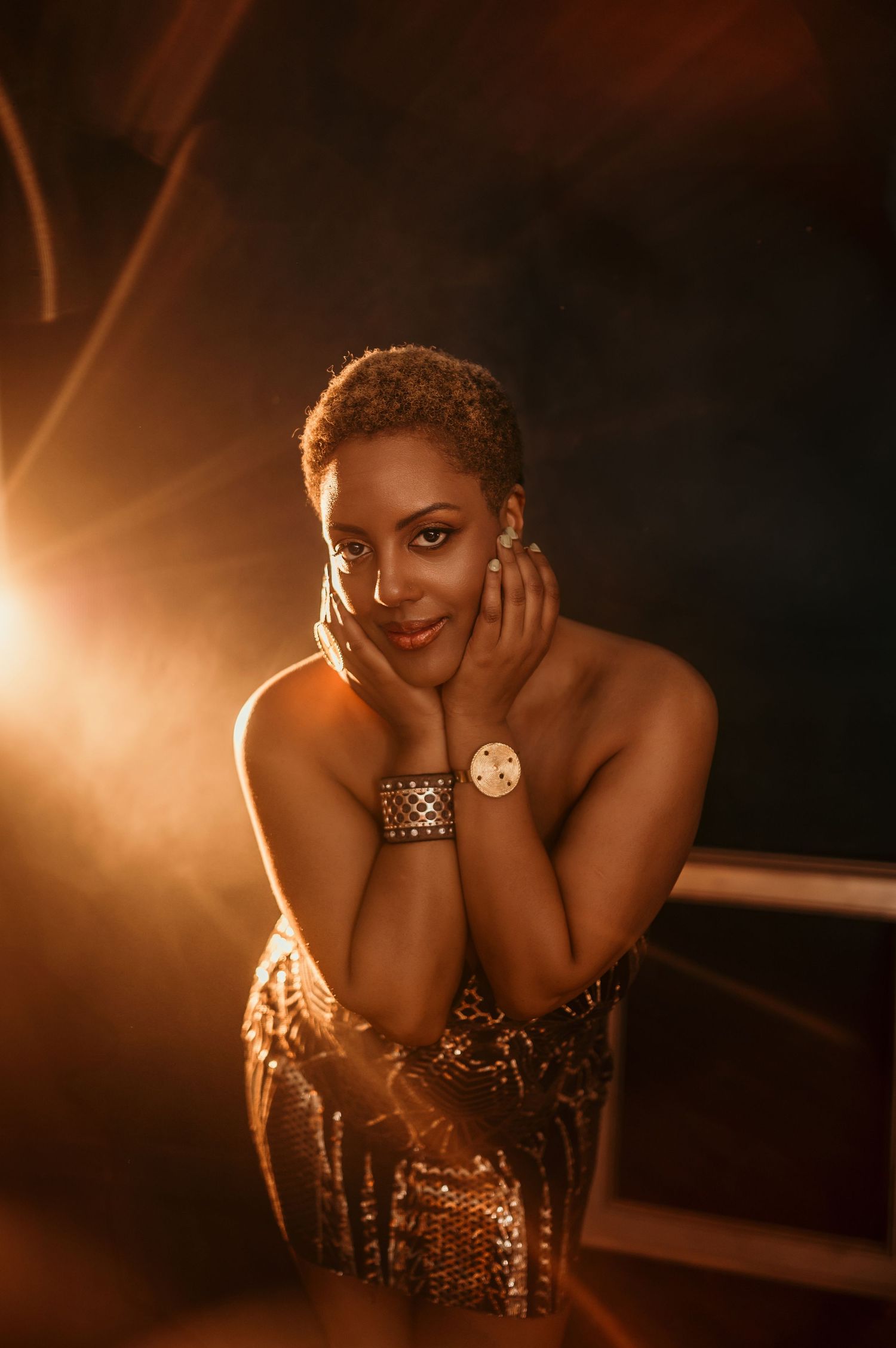 A glamorous portrait in warm lighting shows a figure in a sequined dress with metallic jewelry against a dark background.