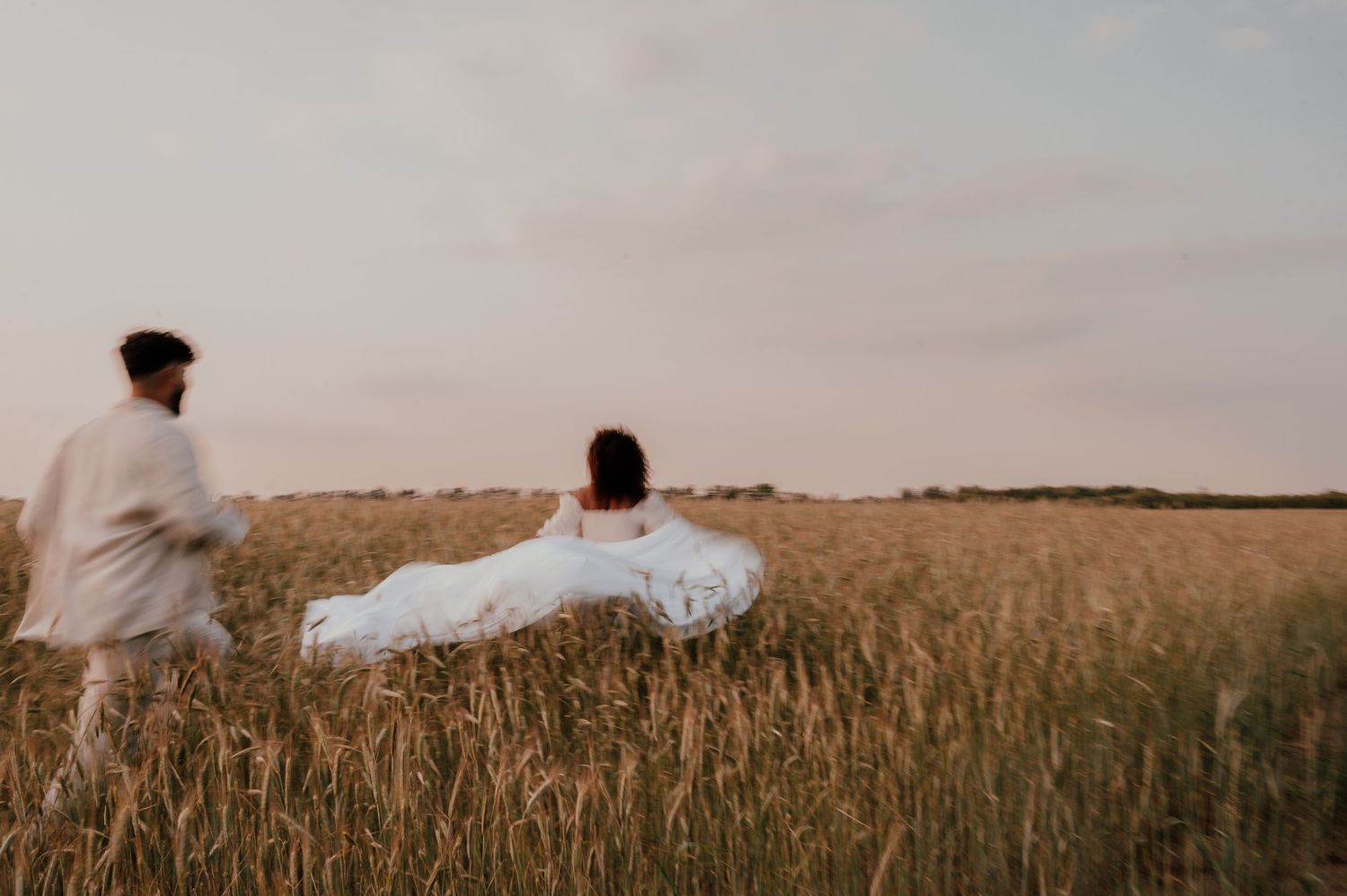 Silhouettes dancing through wheat field at dusk with flowing white fabric.