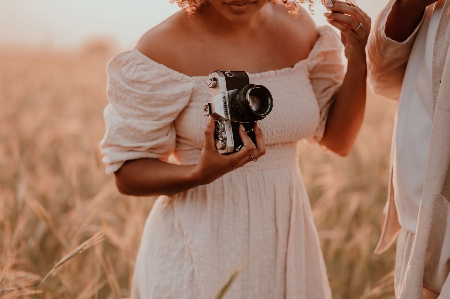 Person in white dress holding vintage camera in wheat field during golden hour.