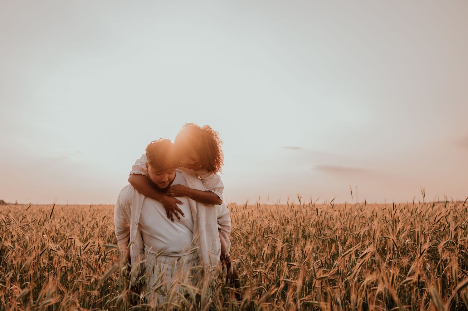 Intimate embrace captured in warm wheat field during sunset.