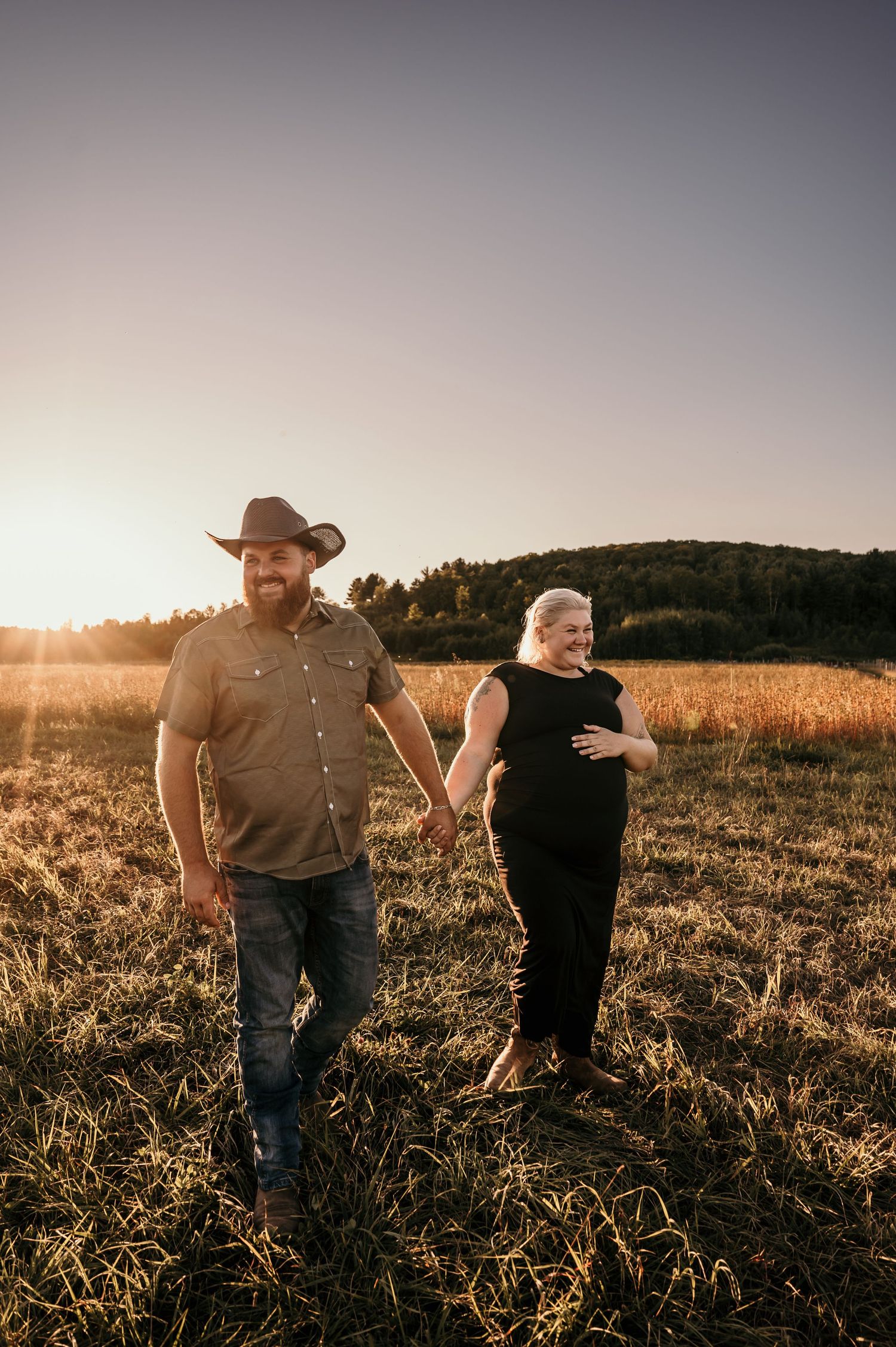 Two people walk through a golden field at sunset, silhouetted against the warm glowing sky.